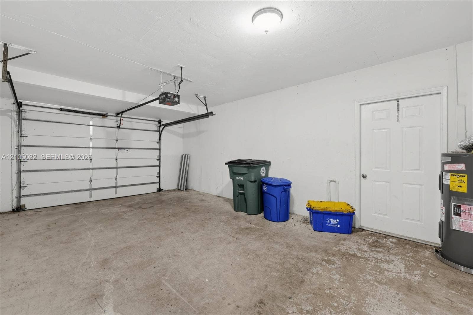 759 NW 7th Street, Boca Raton, FL 33486 Garage featuring a concrete floor, white walls, automated overhead door, and a six-panel pedestrian door