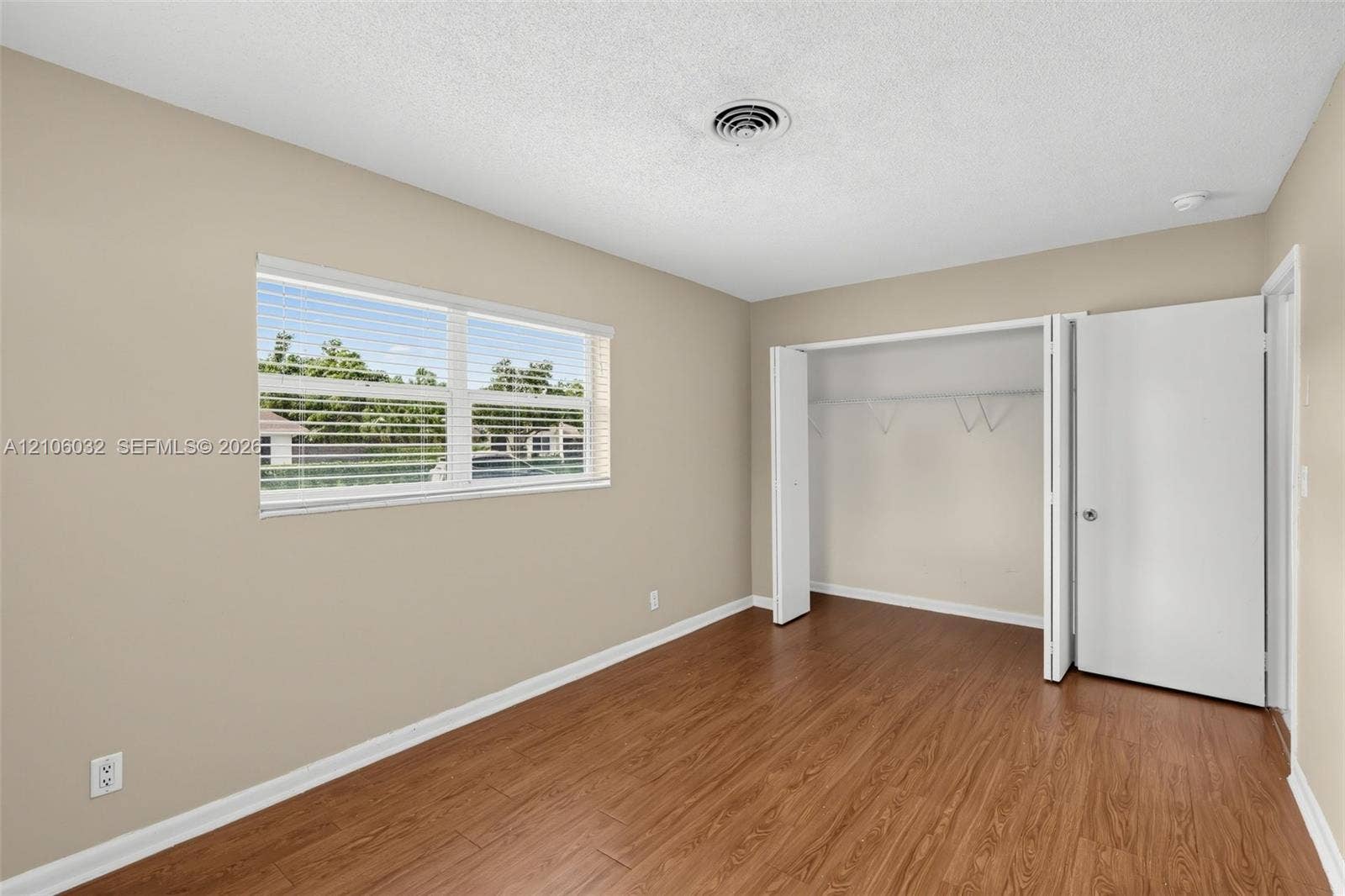 759 NW 7th Street, Boca Raton, FL 33486 Room featuring wood-finish flooring, a large window with horizontal blinds, neutral wall paint, and a built-in closet with folding doors