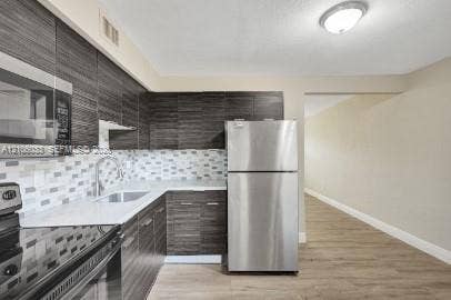 1471 NW 22nd Court, #2, Fort Lauderdale, Fort Lauderdale, FL 33311 Kitchen featuring dark wood-finish cabinetry, solid surface countertops, stainless steel appliances, a multi-tonal mosaic tile backsplash, and wood-finish flooring