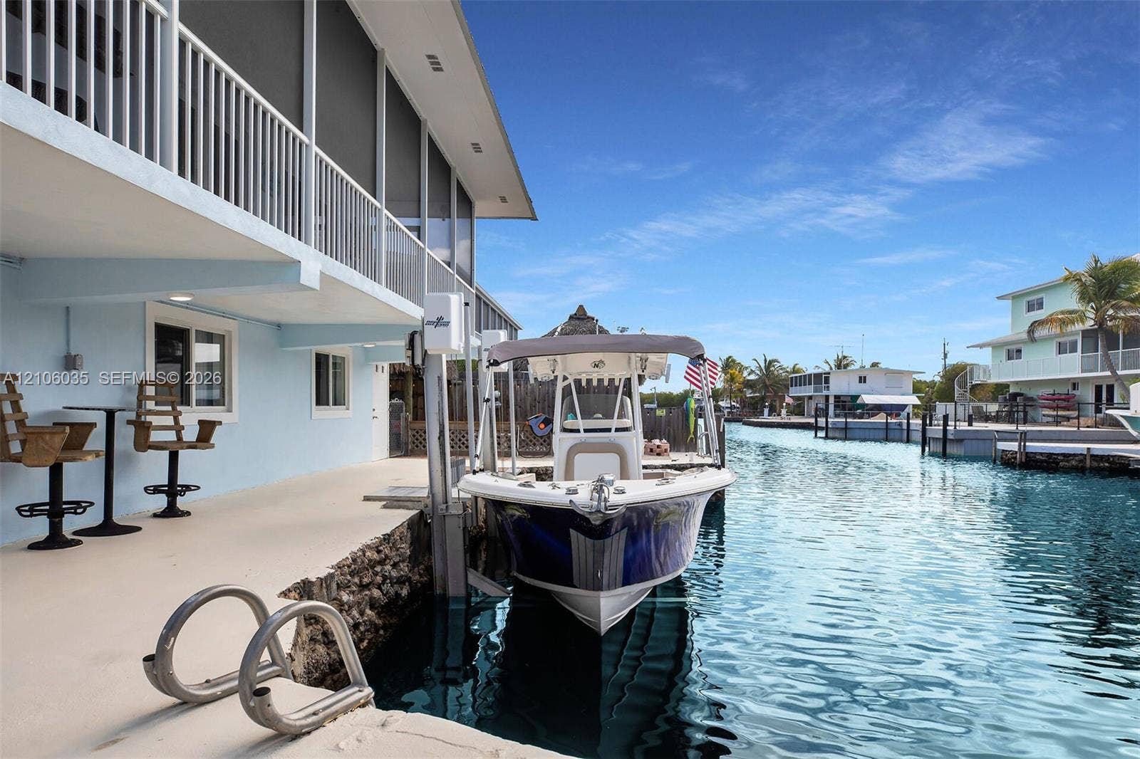 128 Dove Avenue, Tavernier, FL 33070 Waterfront property featuring a concrete seawall, private boat lift, and a covered lower-level concrete patio