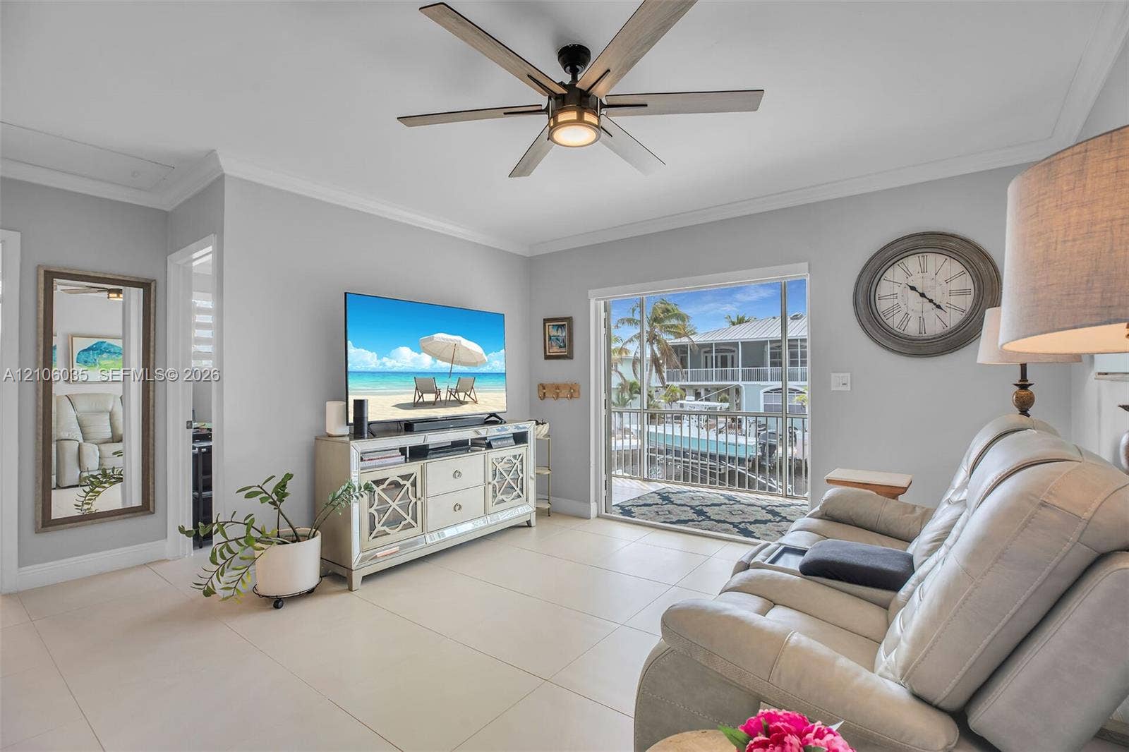128 Dove Avenue, Tavernier, FL 33070 Living area featuring large-format tile flooring, a multi-blade ceiling fan with integrated lighting, crown molding, and sliding glass doors opening to a balcony