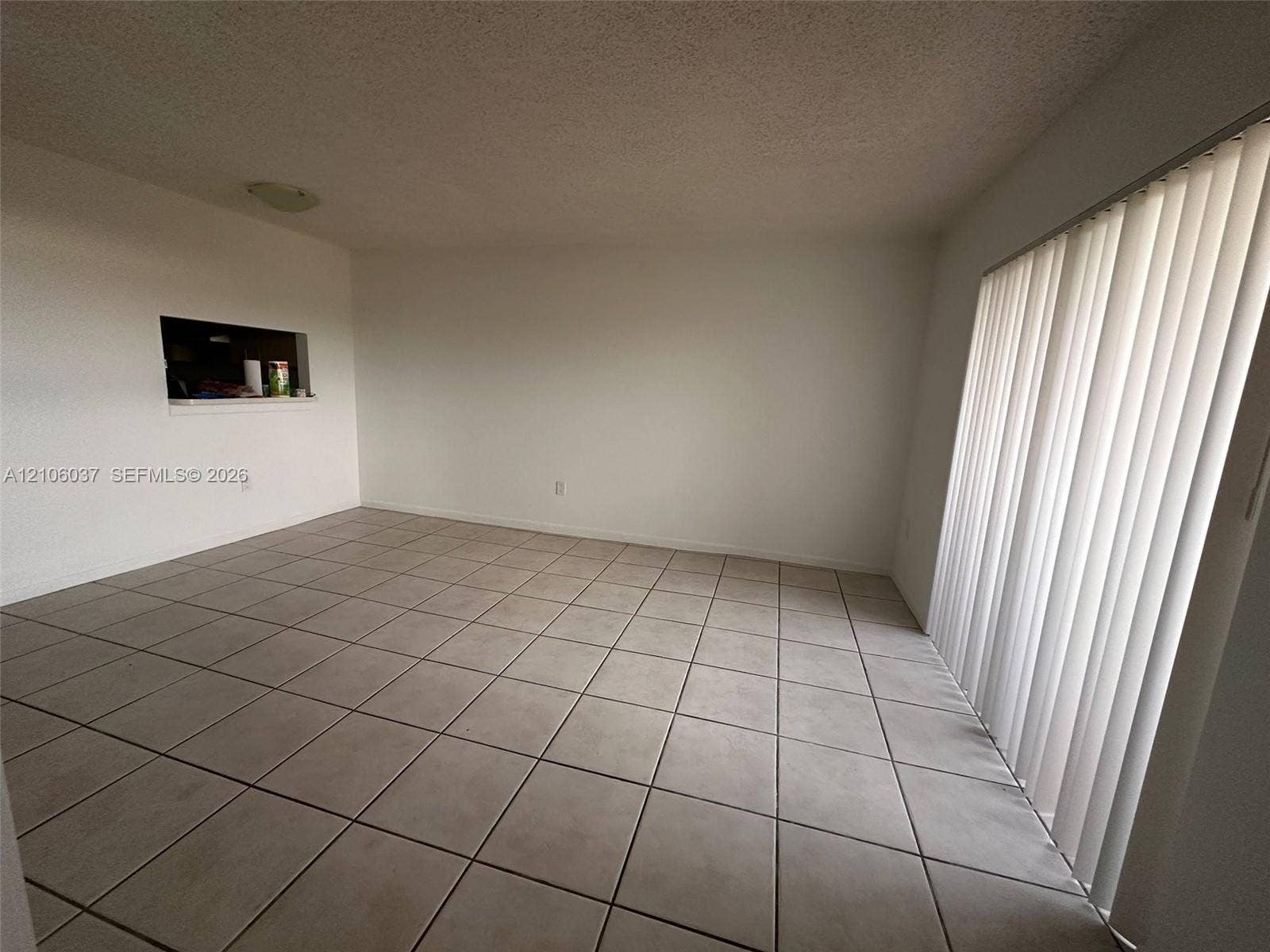 14951 SW 82nd Lane, #17-504, Miami, FL 33193 Room featuring neutral tile flooring, vertical window blinds, and a built-in wall pass-through
