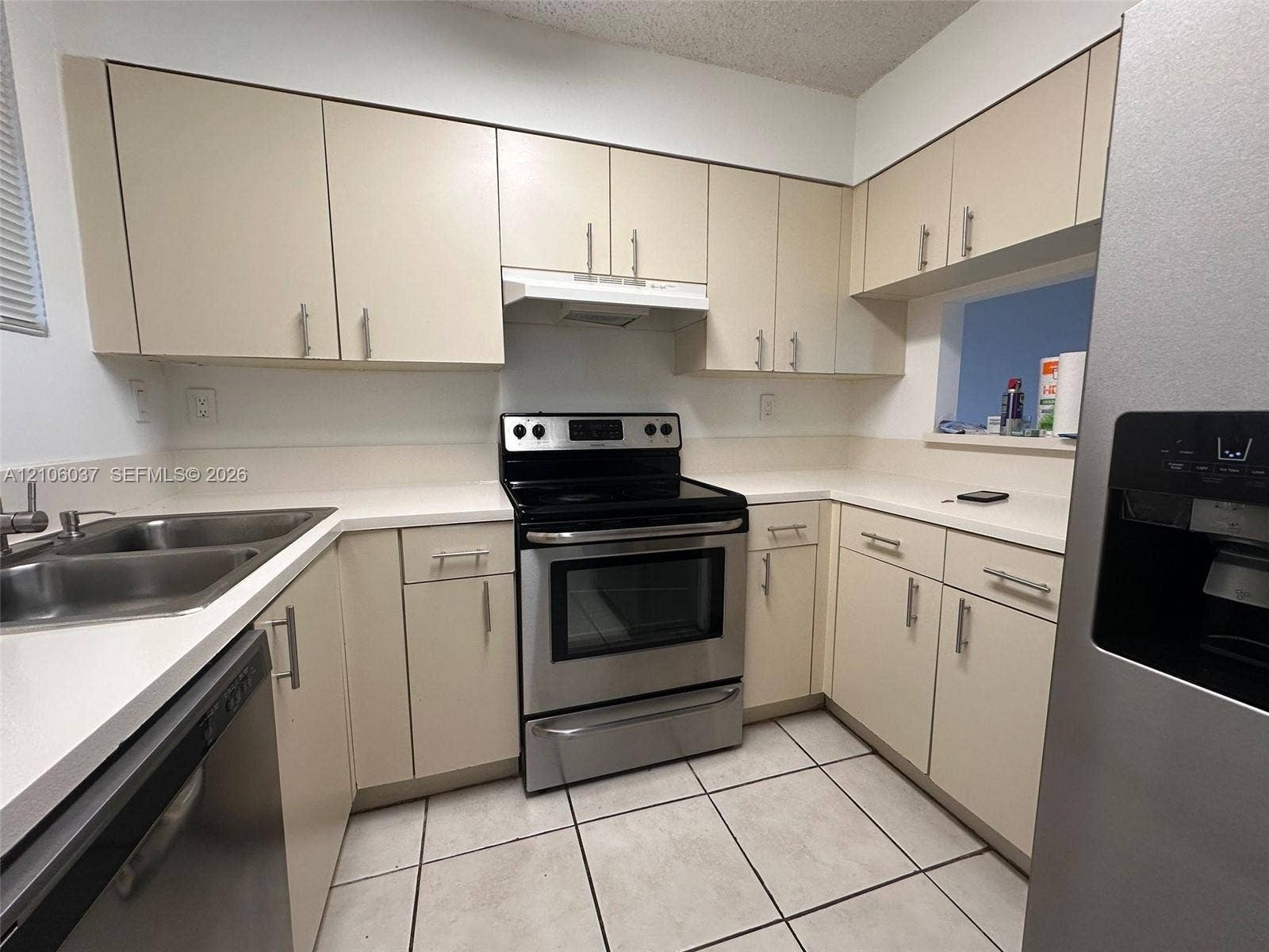 14951 SW 82nd Lane, #17-504, Miami, FL 33193 Kitchen featuring cream-toned cabinetry with metal hardware, solid-surface countertops, stainless steel appliances, a dual-basin sink, and tile flooring
