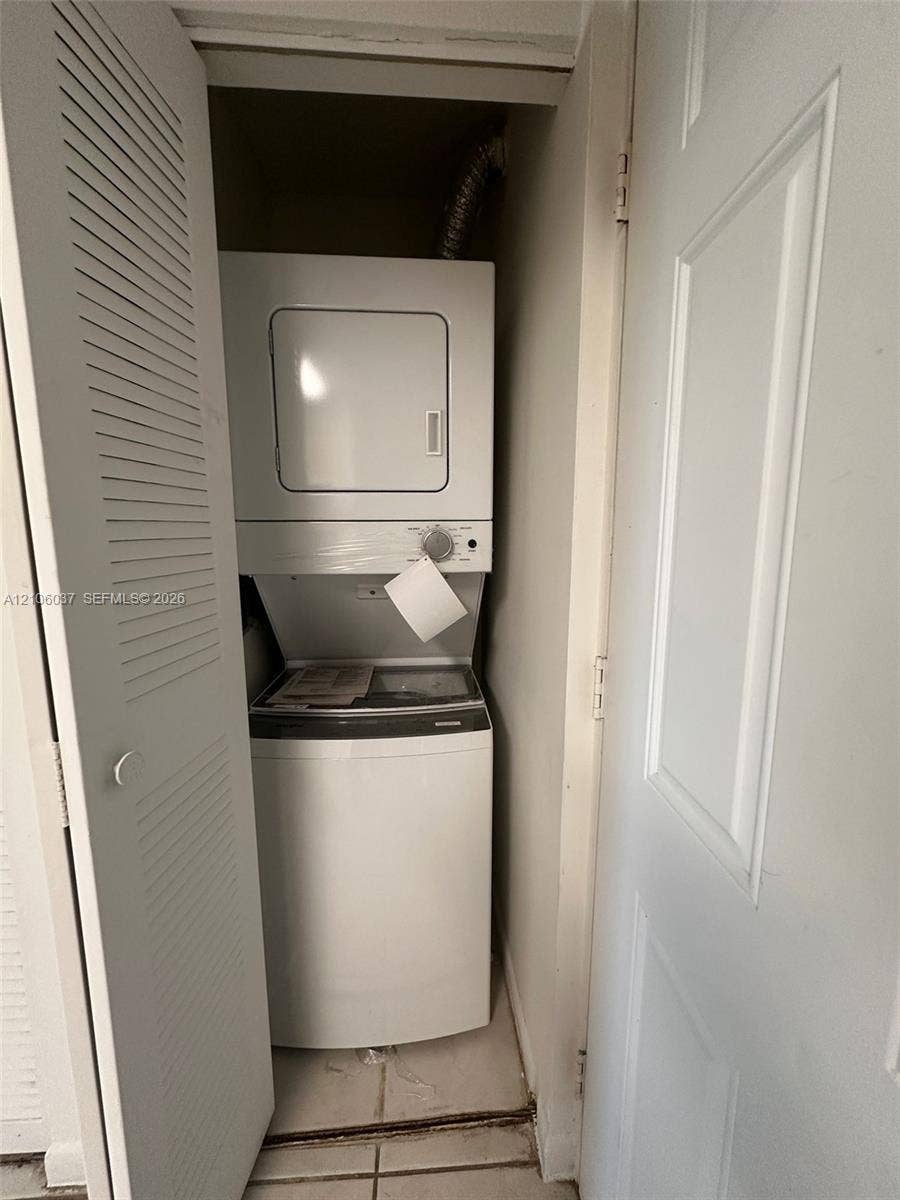 14951 SW 82nd Lane, #17-504, Miami, FL 33193 Laundry closet featuring a white stacked washer and dryer unit, louvered closet doors, and tile flooring