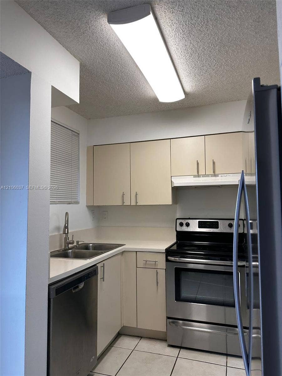 14951 SW 82nd Lane, #17-504, Miami, FL 33193 Kitchen featuring stainless steel appliances, double-basin sink with high-arc faucet, solid-surface countertops, flat-panel cabinetry, and tile flooring