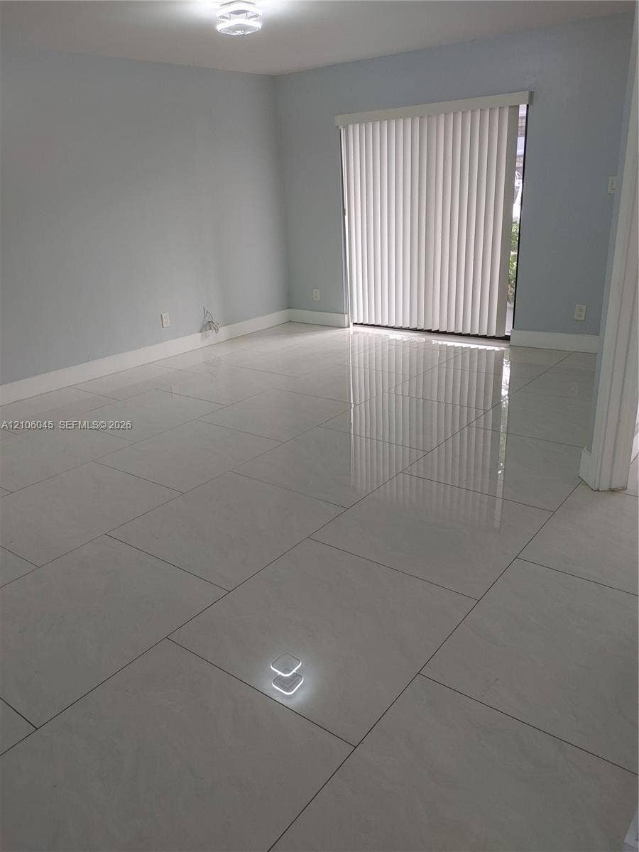 Neutral-toned interior featuring large-format polished tile flooring, light-reflective surfaces, a sliding glass door, and a flush-mount ceiling light fixture