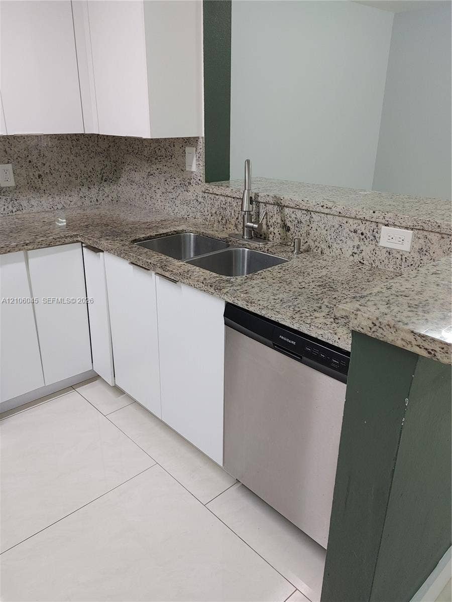 Kitchen featuring white cabinetry, stone countertops, double-basin stainless steel sink with high-arc faucet, stainless steel dishwasher, and large-format tile flooring