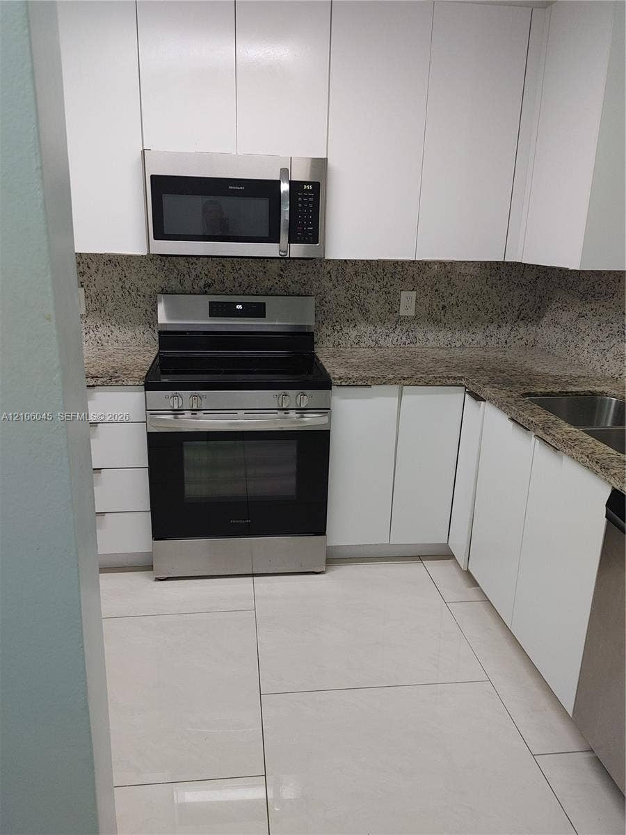 Kitchen featuring white flat-panel cabinetry, stone countertops, stainless steel appliances, and large-format tile flooring
