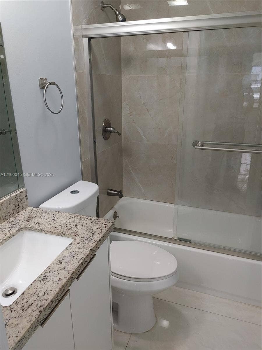 Bathroom featuring a vanity with stone-finish countertop and undermount sink, shower-tub combination with glass sliding doors, and large-format tile surround