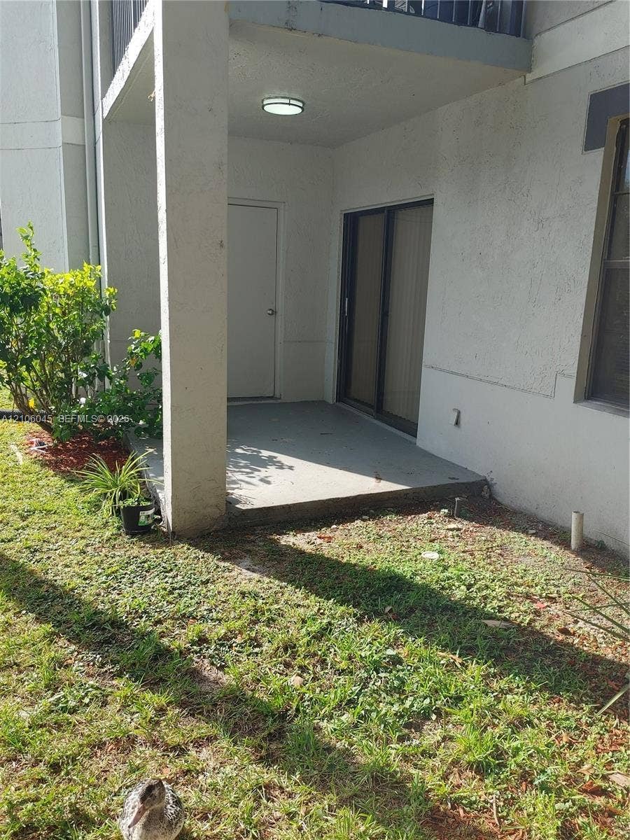 Covered ground-level patio featuring a concrete floor, integrated storage closet, sliding glass door, and overhead lighting