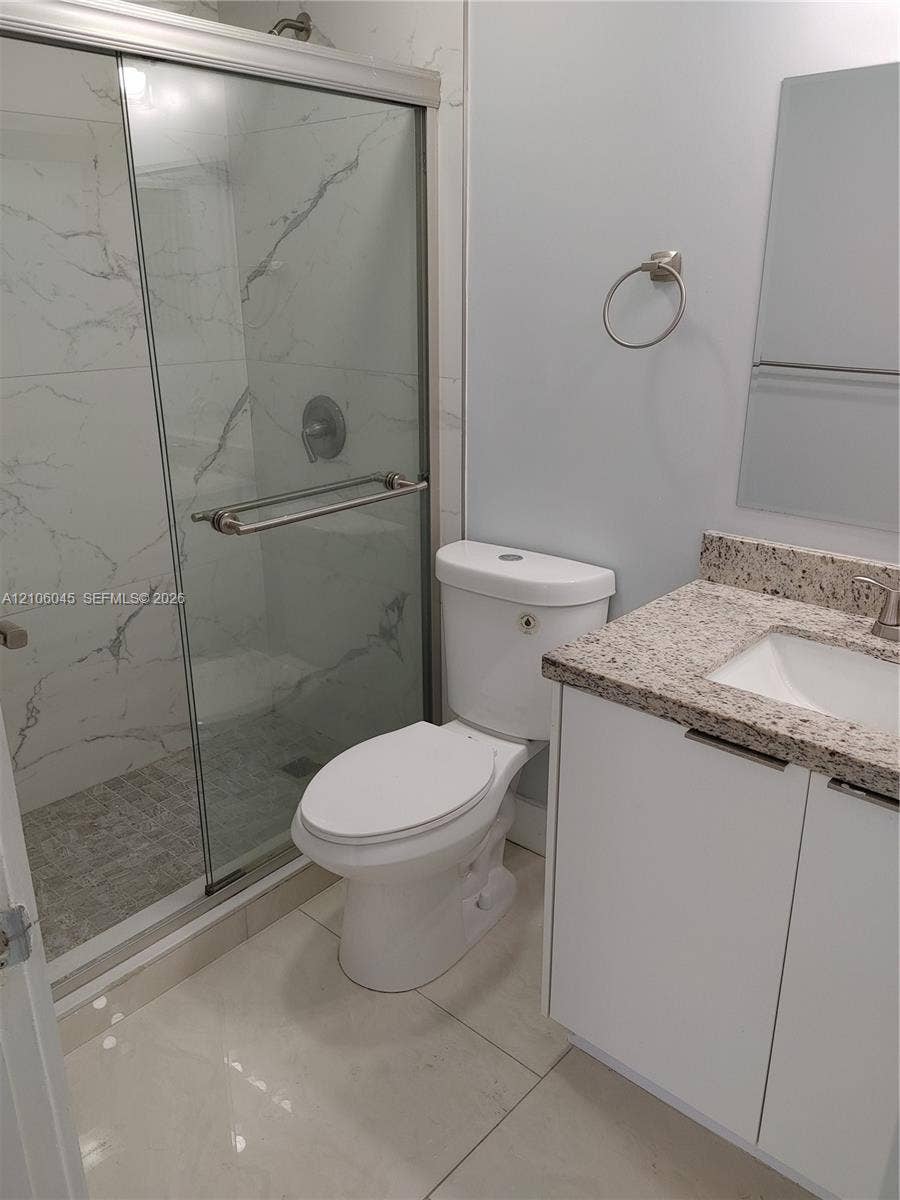 Walk-in shower with floor-to-ceiling large-format tile surround, frameless glass door, vanity with speckled stone-finish countertop, and polished chrome fixtures