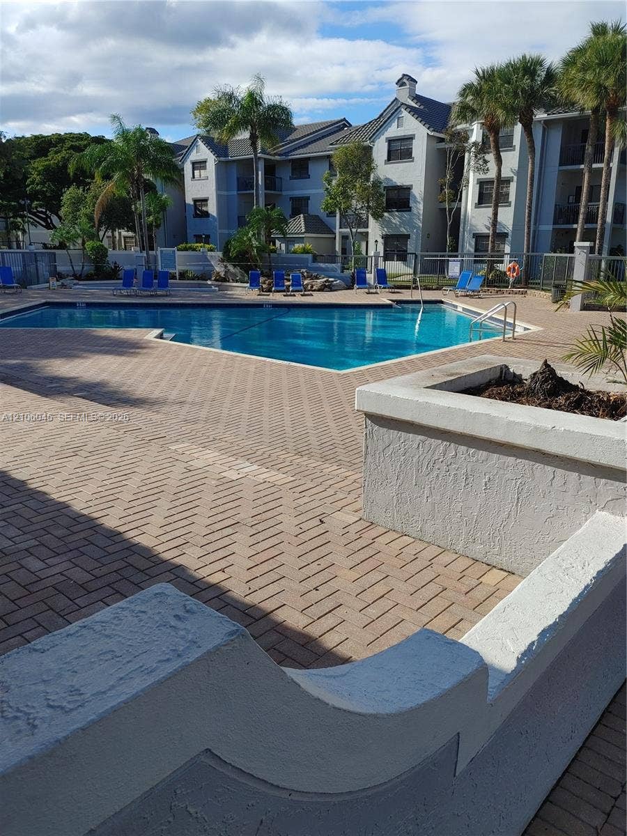In-ground pool surrounded by a herringbone-pattern brick paver deck, stucco-finished retaining walls, and mature palm trees