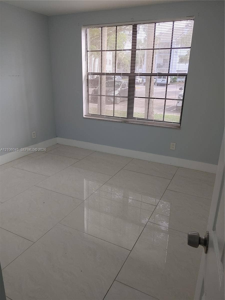 Large-format tile flooring, neutral wall paint, and a grid-pane window featuring installed blinds