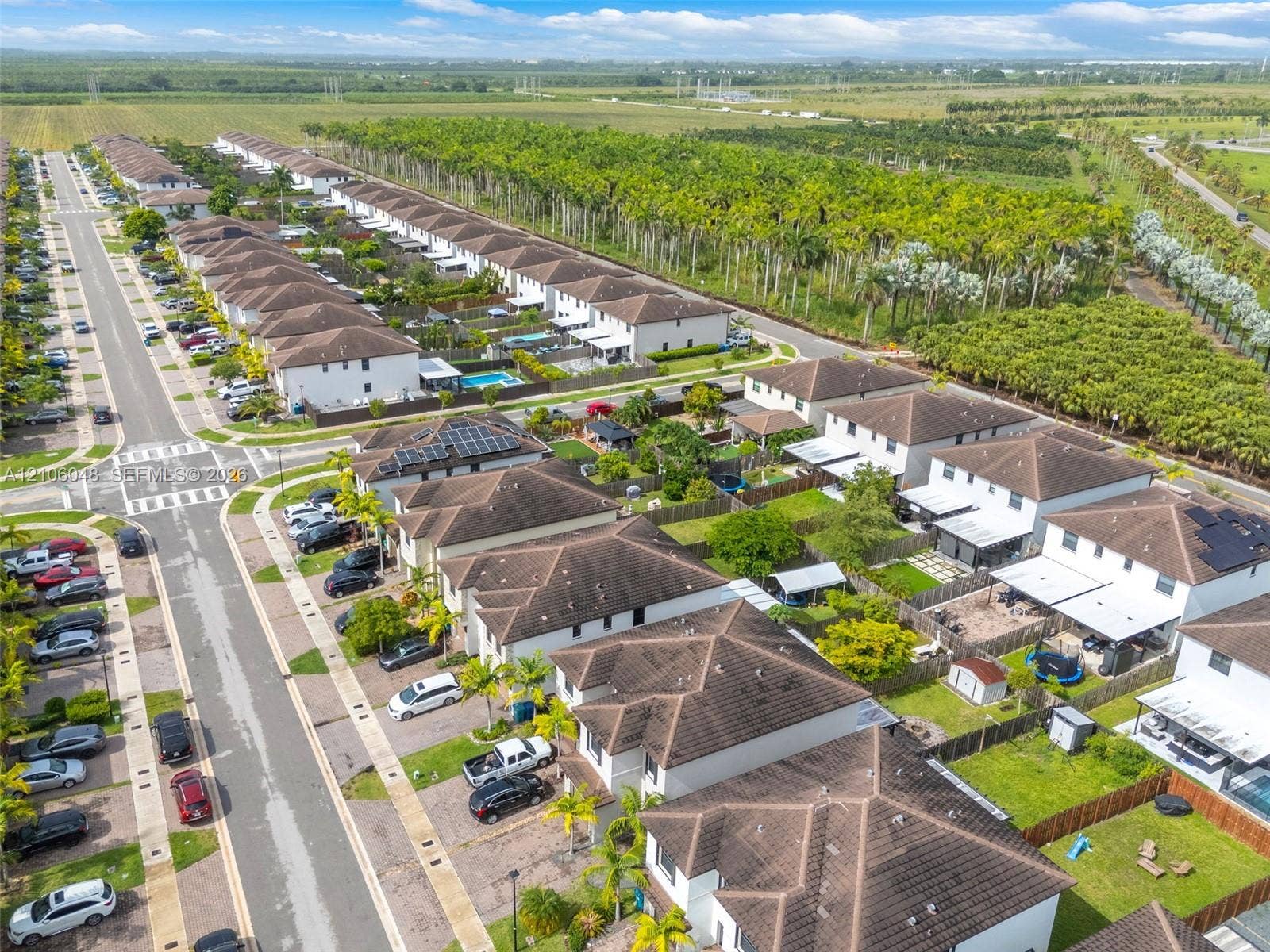 25134 SW 108th Court, Homestead, FL 33032 Aerial perspective of a planned community featuring multi-level residential structures, shingle rooflines, integrated solar energy panels, paved thoroughfares, and bordering natural vegetation