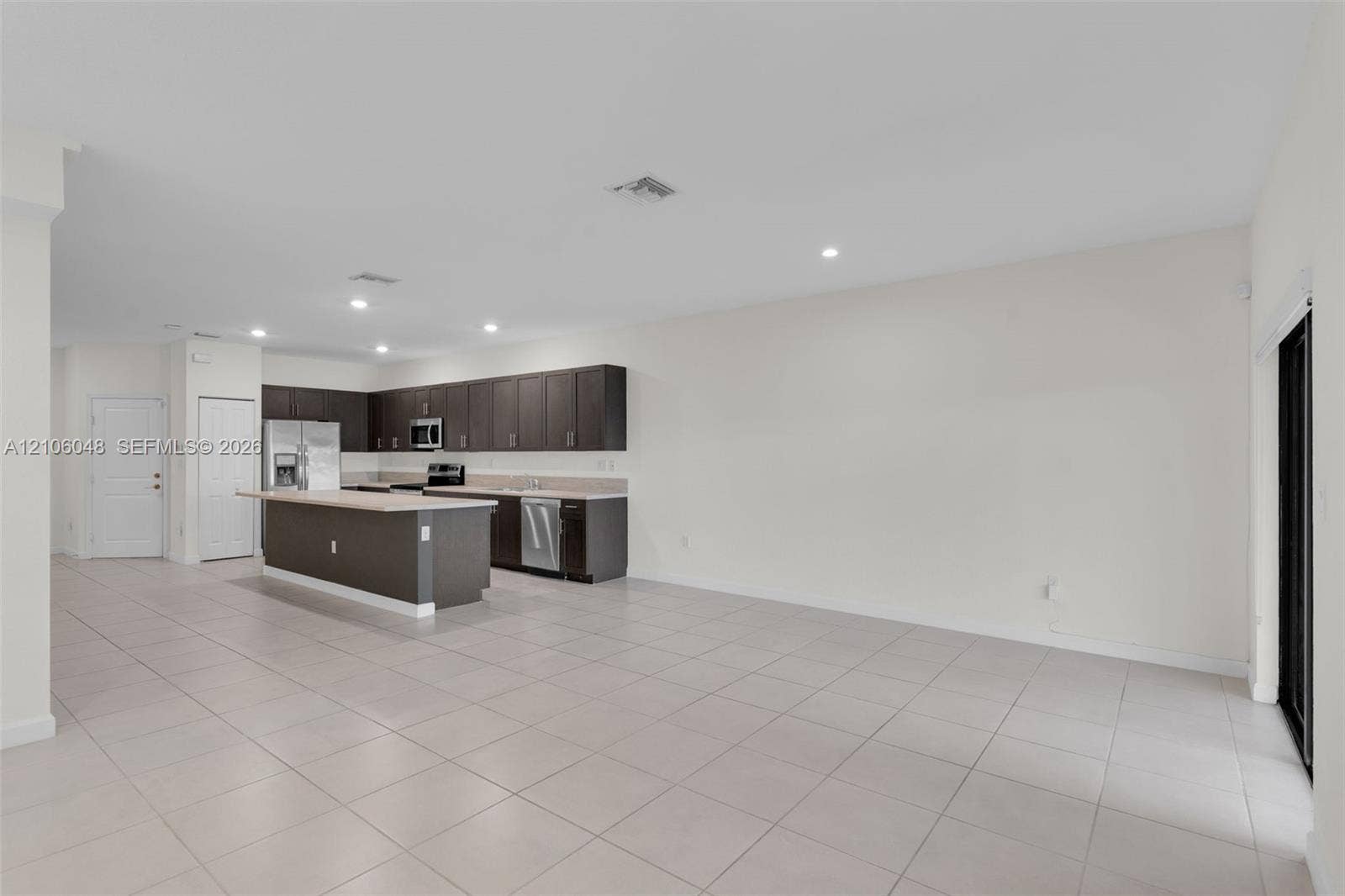 25134 SW 108th Court, Homestead, FL 33032 Open-concept kitchen featuring dark espresso cabinetry, a central island with countertop seating, stone-finish countertops, stainless steel appliances, and large-format tile flooring