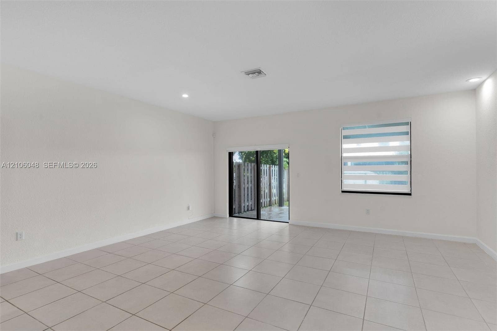 25134 SW 108th Court, Homestead, FL 33032 Neutral-toned interior space featuring light-colored ceramic tile flooring, recessed ceiling lighting, a single window with horizontal zebra-style blinds, and a sliding glass door