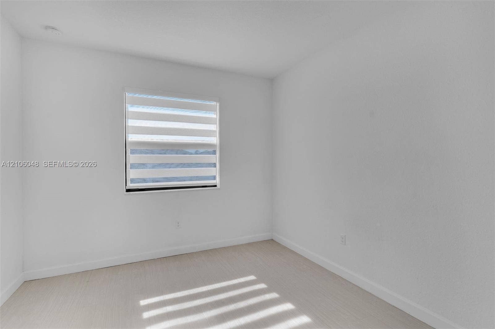 25134 SW 108th Court, Homestead, FL 33032 Neutral interior featuring crisp white walls, light-toned wood-finish flooring, and a window equipped with horizontal zebra-style blinds
