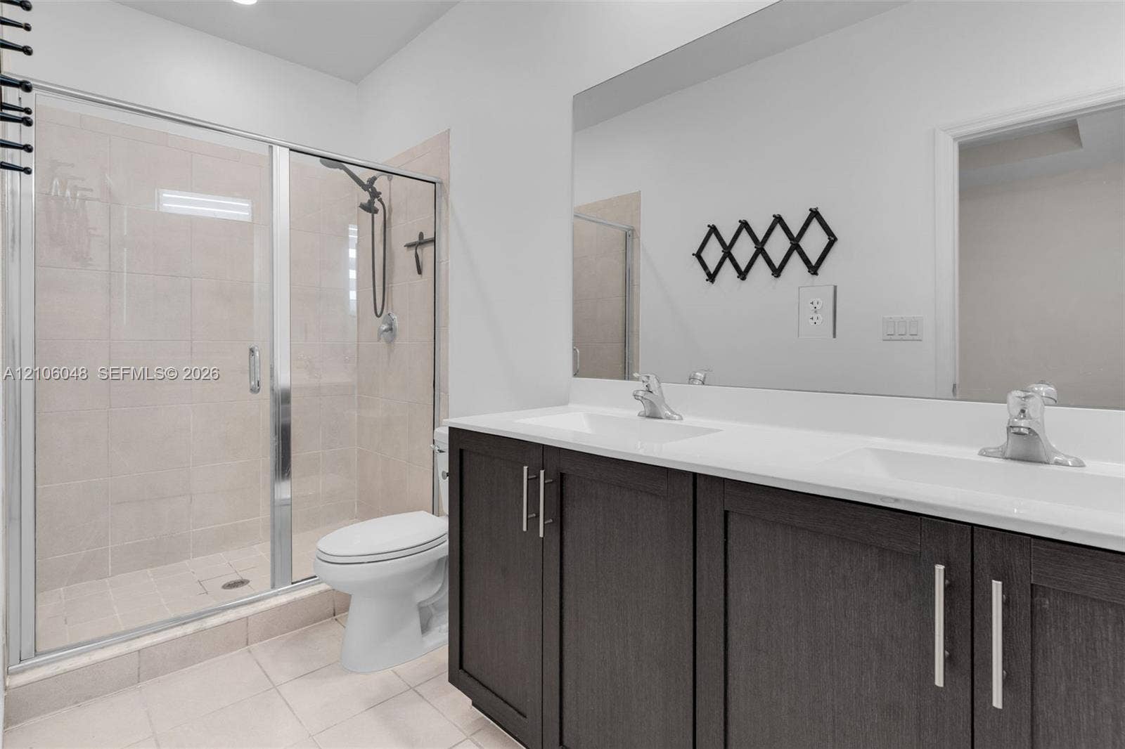 25134 SW 108th Court, Homestead, FL 33032 Double vanity with dark cabinetry, white countertops, integrated sinks, chrome hardware, and a glass-enclosed shower with tiled surround