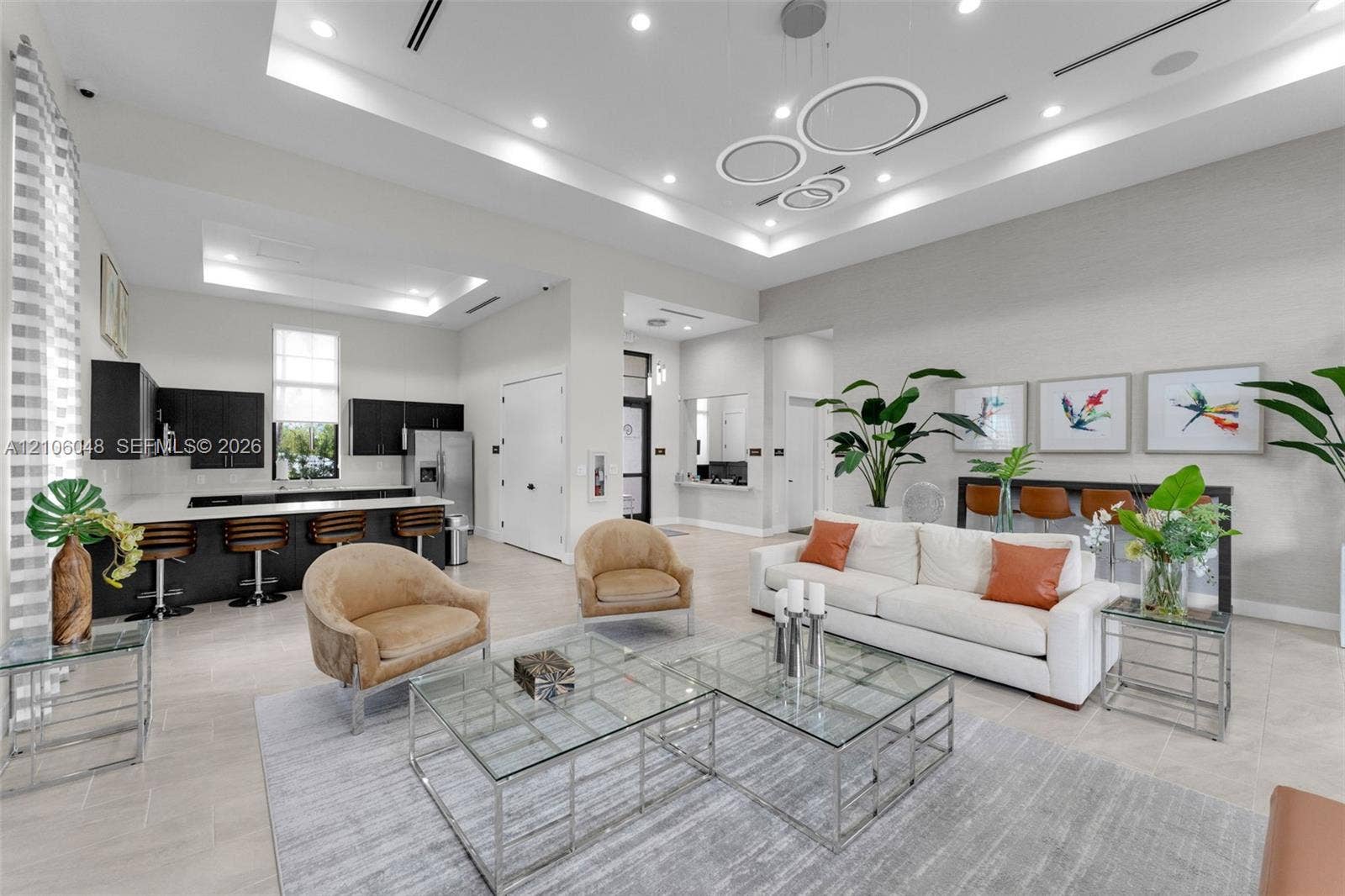 25134 SW 108th Court, Homestead, FL 33032 Open-concept space featuring high tray ceilings with recessed lighting, modern geometric chandelier, tiled flooring, and a kitchen area equipped with dark cabinetry, light-toned countertops, and a breakfast bar