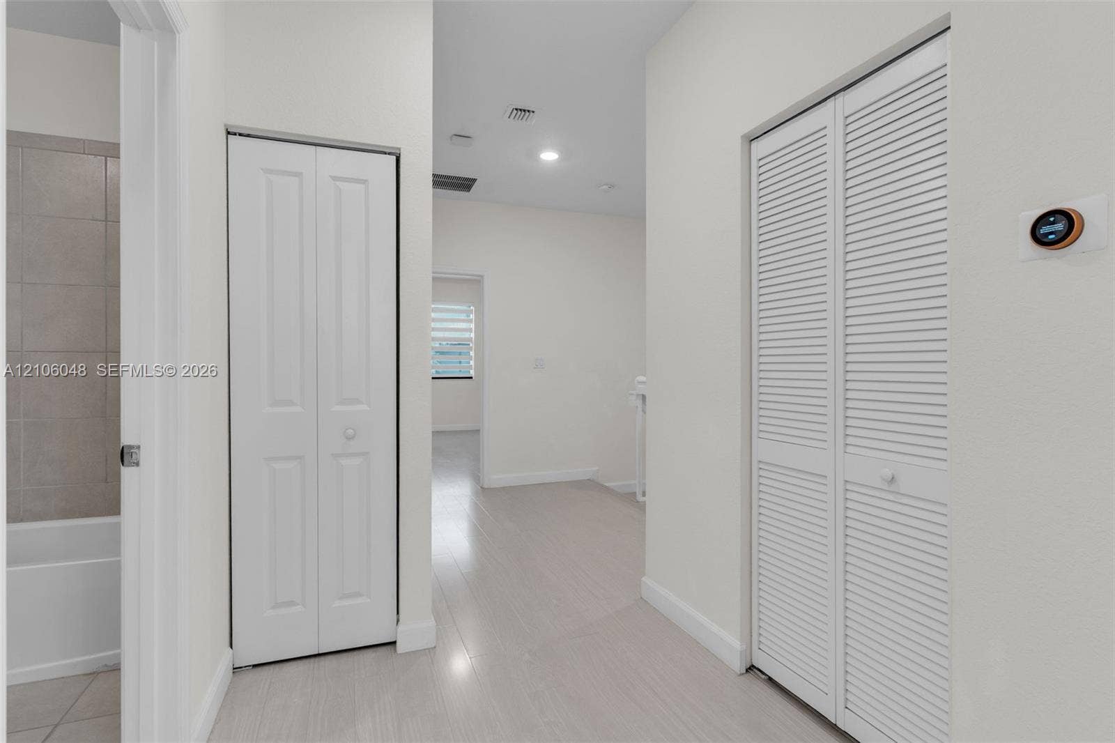 25134 SW 108th Court, Homestead, FL 33032 Hallway featuring wood-finish flooring, two sets of white bifold doors, and a wall-mounted programmable thermostat