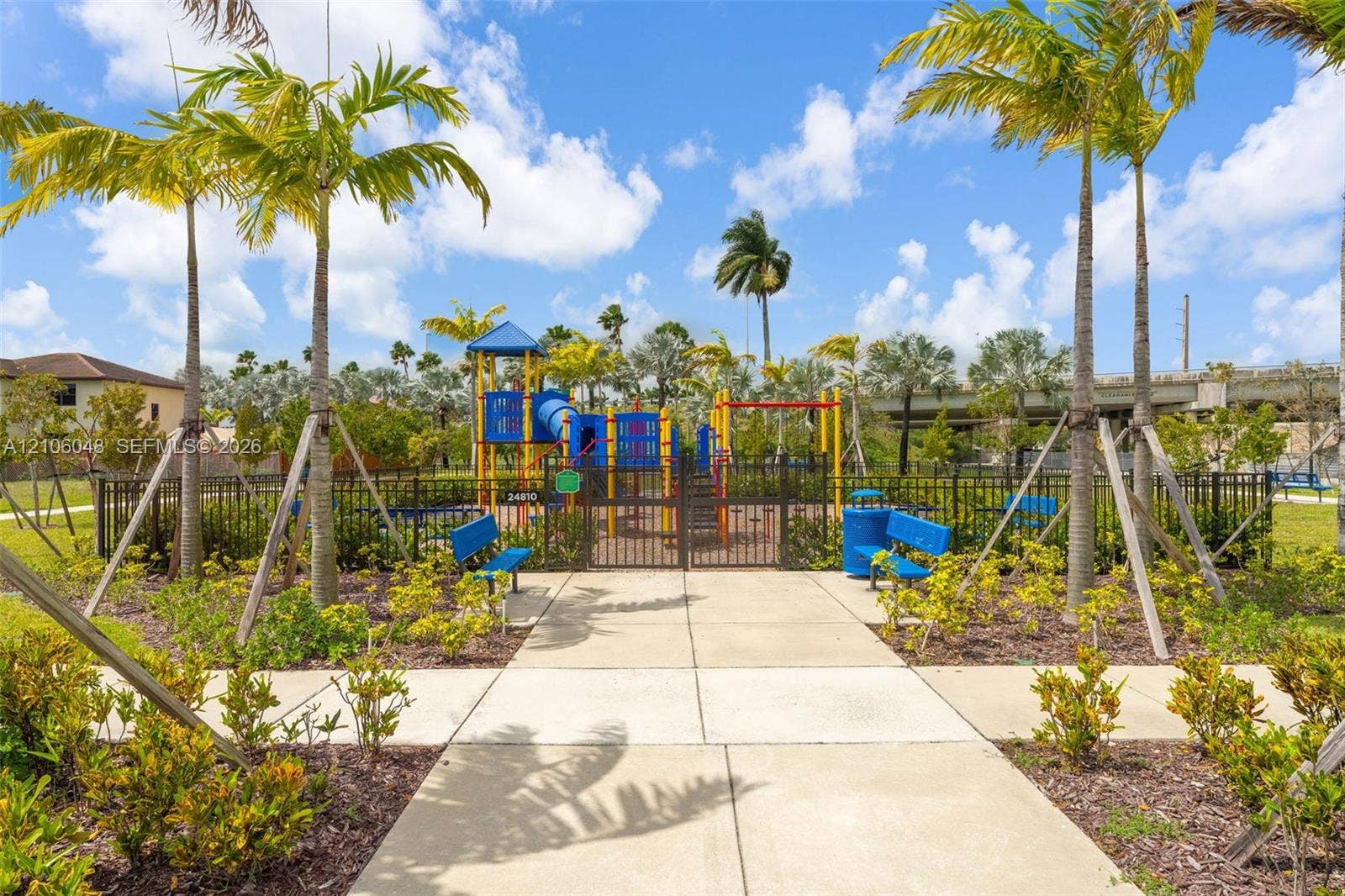 25134 SW 108th Court, Homestead, FL 33032 Fenced recreation area featuring a playground structure, concrete walking paths, built-in benches, and mature palm trees