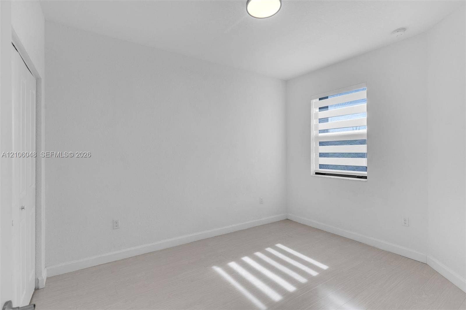 25134 SW 108th Court, Homestead, FL 33032 Bright room featuring neutral wall finishes, light-toned wood-finish flooring, a single window with integrated horizontal blinds, and a white paneled closet door