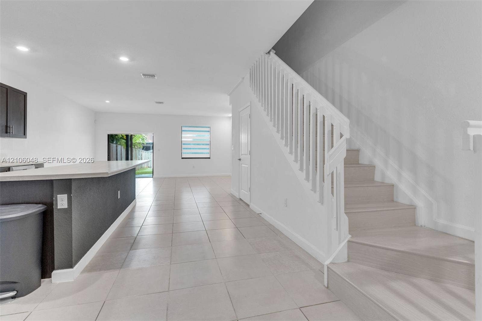 25134 SW 108th Court, Homestead, FL 33032 Interior featuring light-toned tile flooring, a kitchen island with stone-surface countertop, recessed ceiling lighting, and a staircase with white balusters
