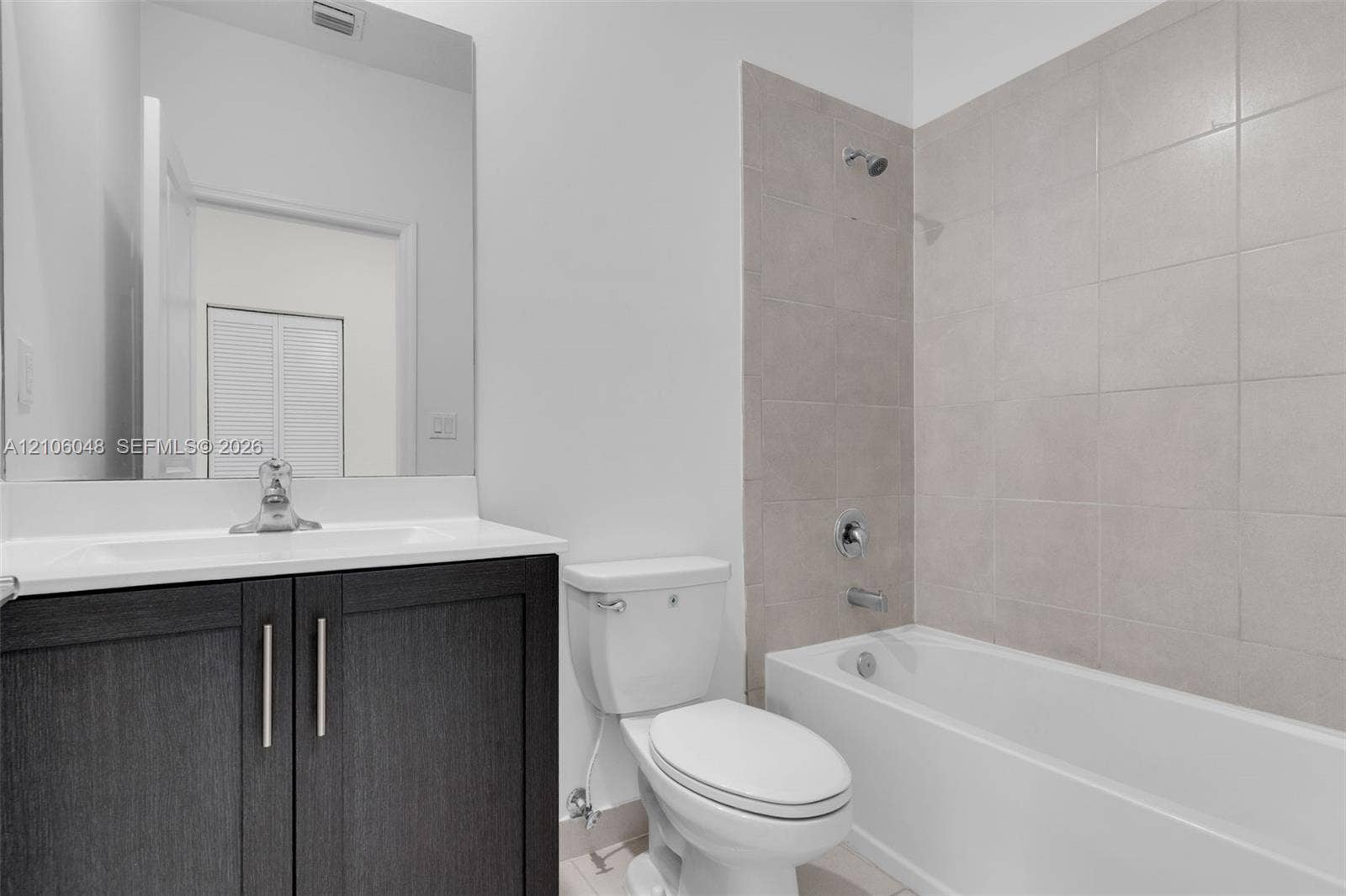 25134 SW 108th Court, Homestead, FL 33032 Dark-finish vanity cabinet with a light-toned countertop, large-format mirror, and bathtub with floor-to-ceiling neutral tile surround