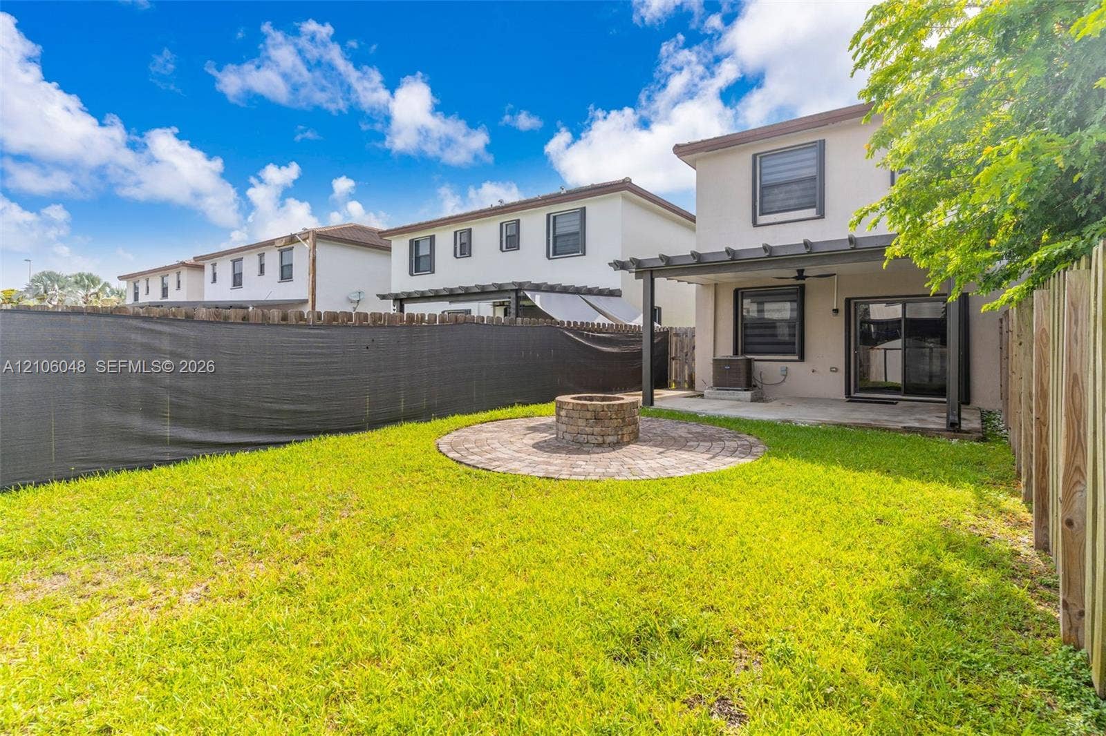 25134 SW 108th Court, Homestead, FL 33032 Fenced backyard featuring a covered concrete patio, a circular paver fire pit area, and a lawn
