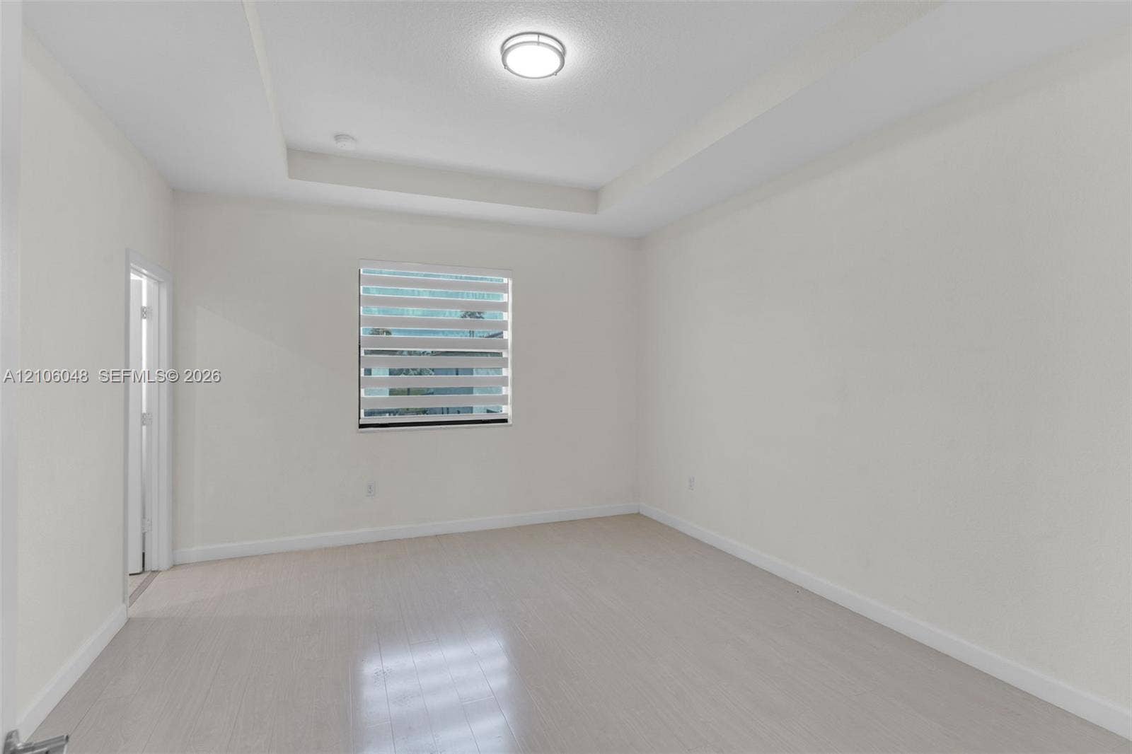 25134 SW 108th Court, Homestead, FL 33032 Room featuring a tray ceiling, light-toned wood-finish flooring, and a window with zebra-style blinds