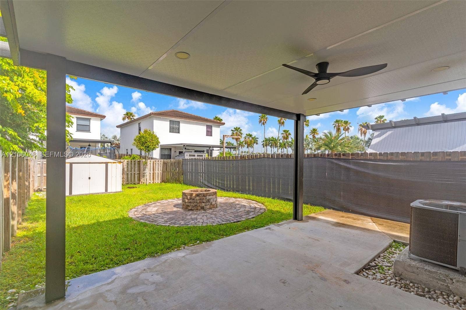 25134 SW 108th Court, Homestead, FL 33032 Covered concrete patio featuring a ceiling fan and recessed lighting, overlooking a fenced backyard with a circular stone fire pit