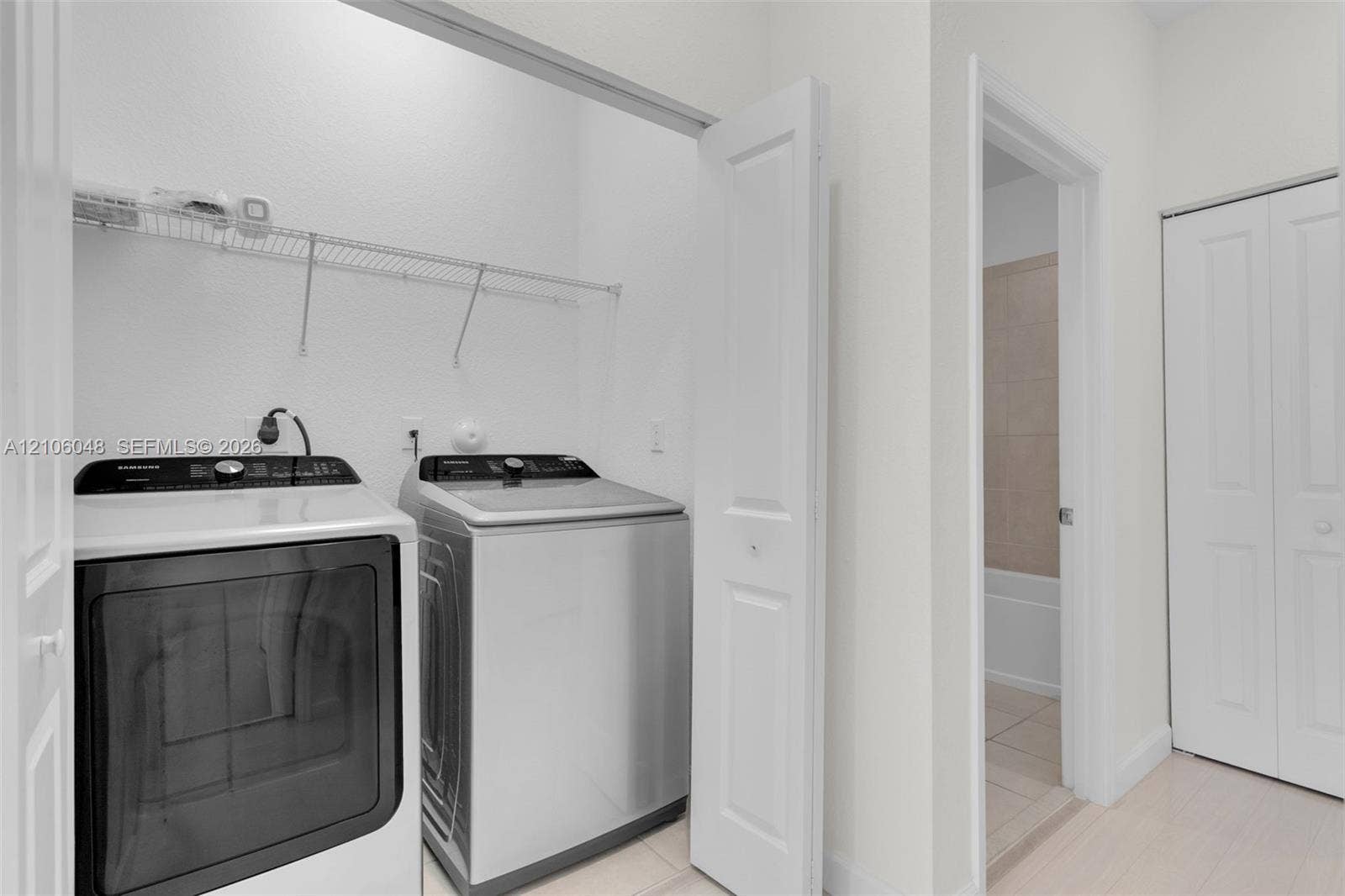 25134 SW 108th Court, Homestead, FL 33032 Utility room featuring stainless steel top-load laundry appliances, white panel doors, overhead wire shelving, and neutral tile flooring