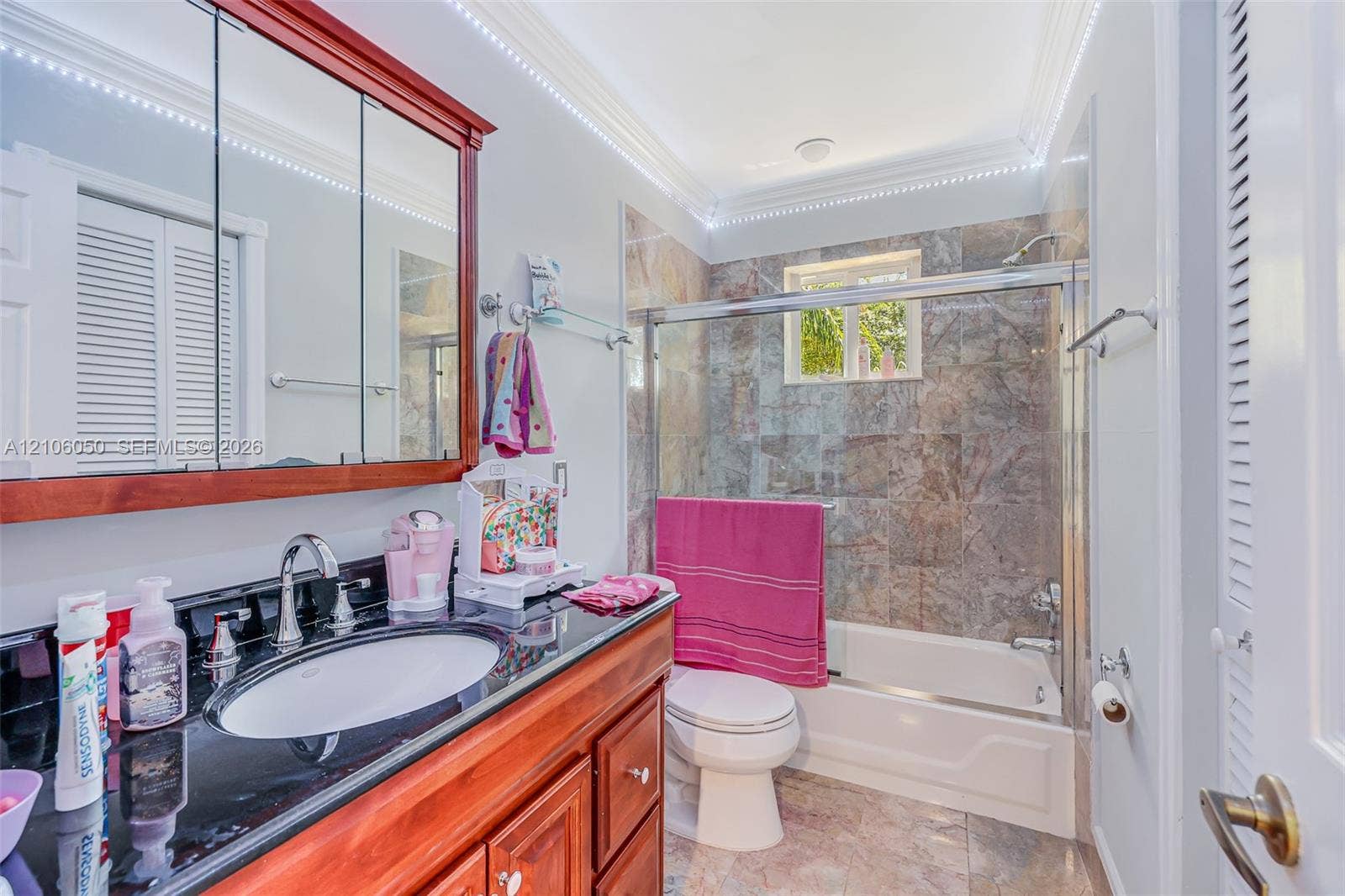 1065 Weeping Willow Way, #0, Hollywood, Hollywood, FL 33019 Bathroom featuring a wood-finish vanity with a dark polished countertop, undermount sink, multi-panel medicine cabinet, and a bathtub enclosure with stone-patterned tile surround