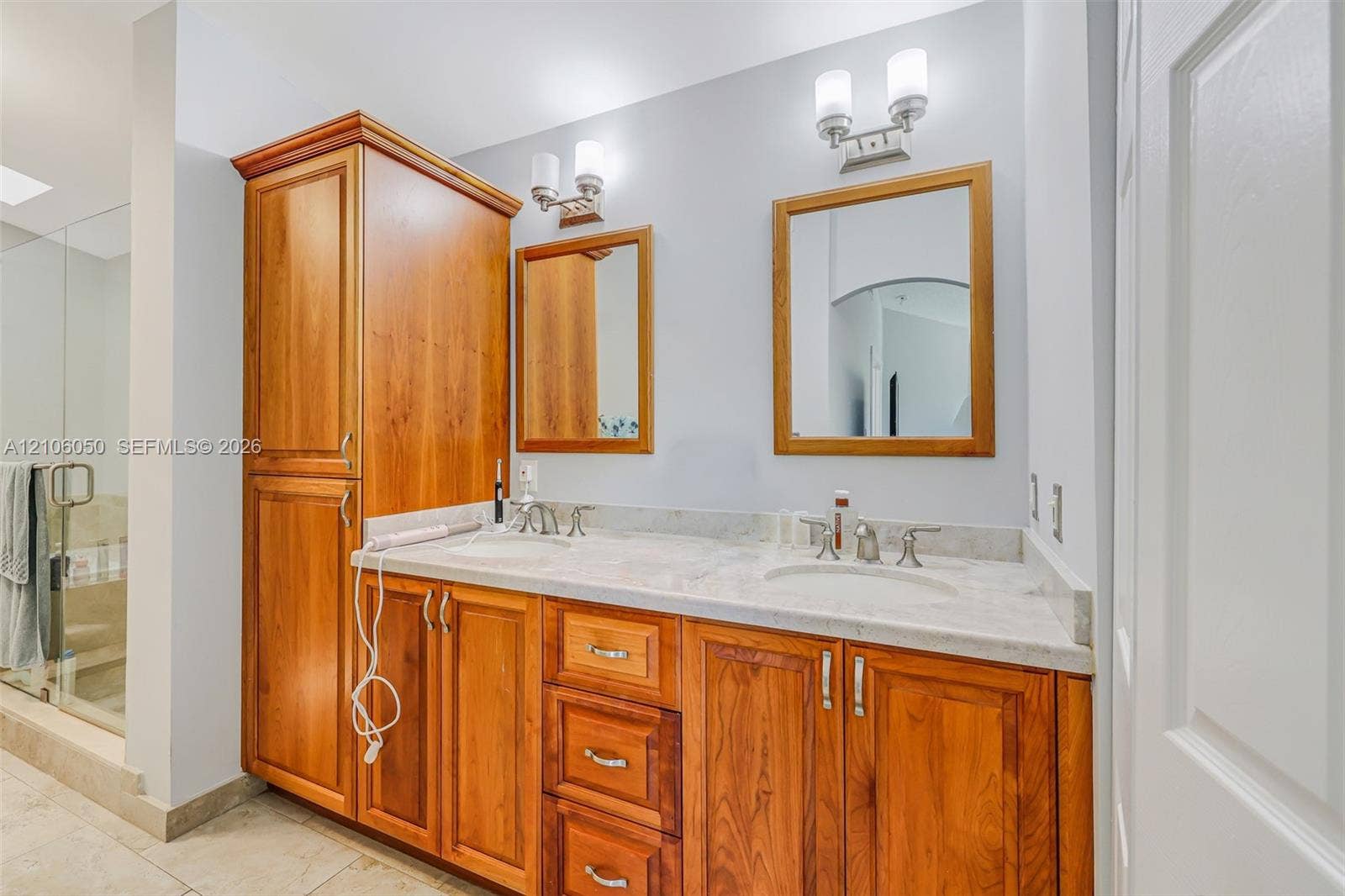 1065 Weeping Willow Way, #0, Hollywood, Hollywood, FL 33019 Double vanity featuring a light-toned stone countertop, wood cabinetry with integrated floor-to-ceiling storage, two wall-mounted mirrors with wood frames, and dual brushed-nickel wall sconces