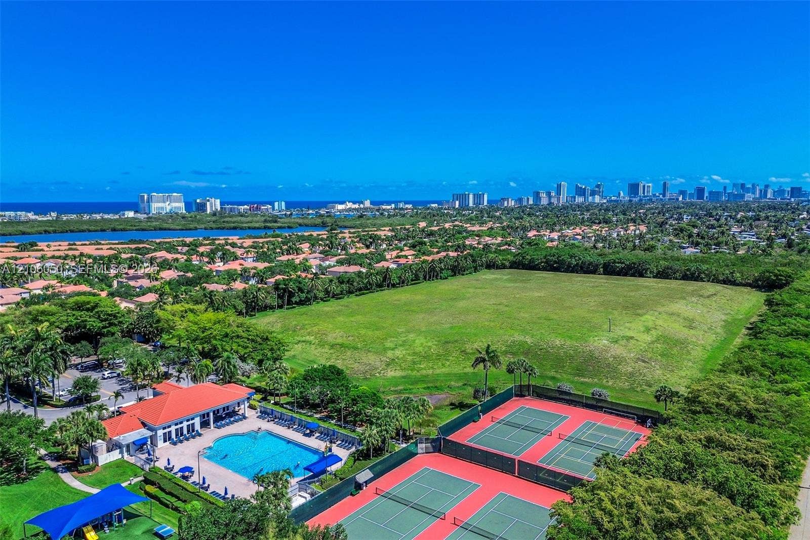1065 Weeping Willow Way, #0, Hollywood, Hollywood, FL 33019 Aerial perspective featuring a clubhouse, an outdoor swimming pool with a surrounding paved deck, and two hard-surface tennis courts
