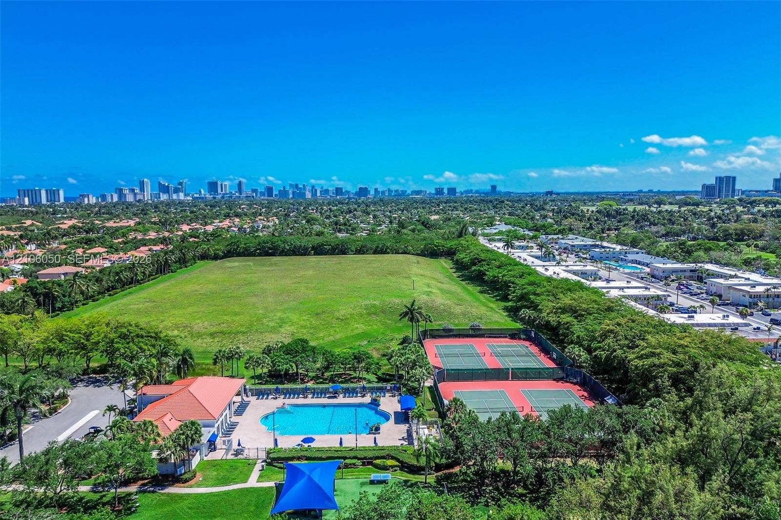 1065 Weeping Willow Way, #0, Hollywood, Hollywood, FL 33019 Expansive outdoor recreational complex featuring two fenced tennis courts, a swimming pool with paved deck, and a clubhouse with a clay-tile roof