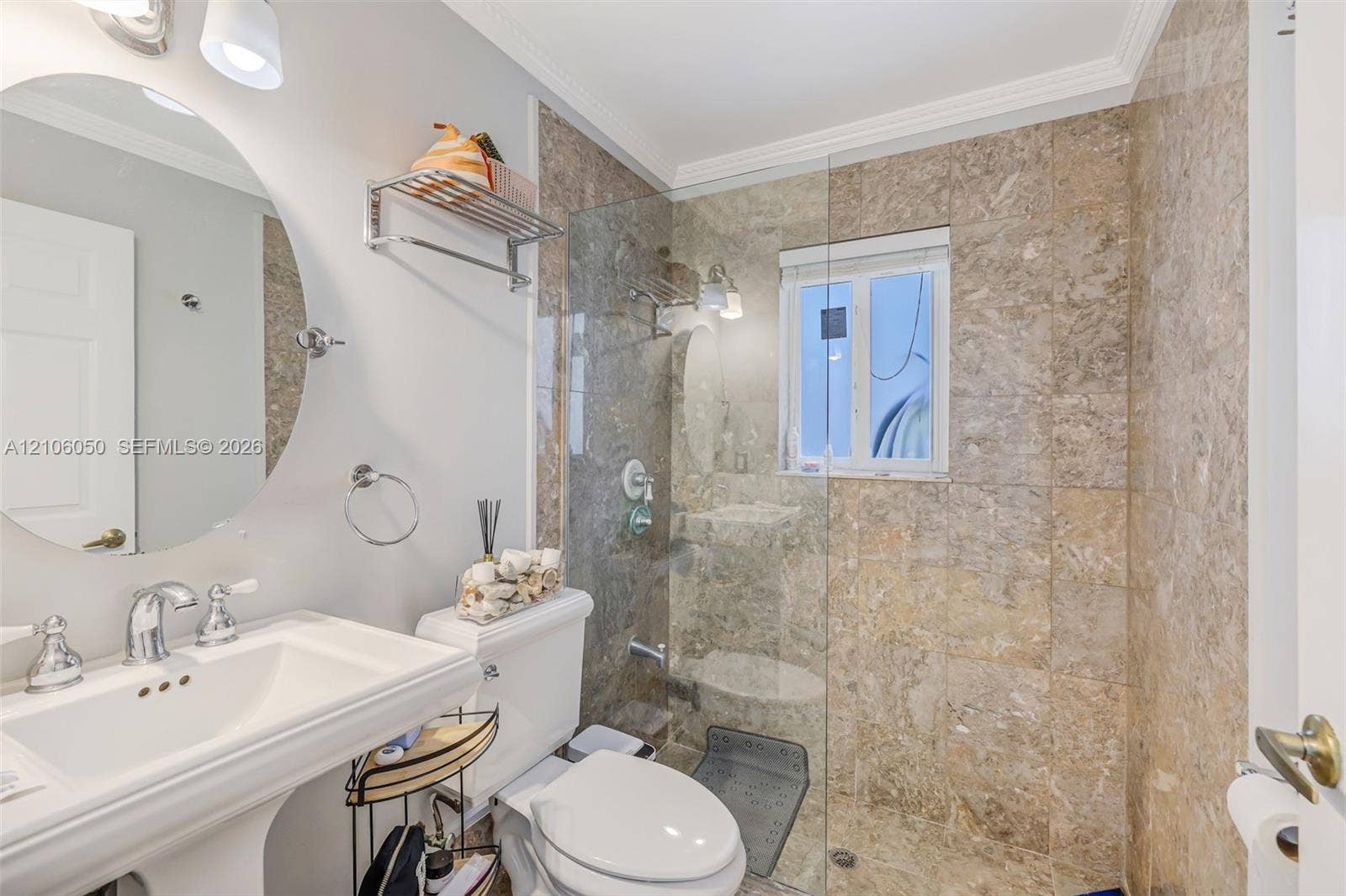 1065 Weeping Willow Way, #0, Hollywood, Hollywood, FL 33019 Pedestal sink with chrome faucet, oval wall-mounted mirror, and walk-in shower featuring glass enclosure and natural stone tile surround