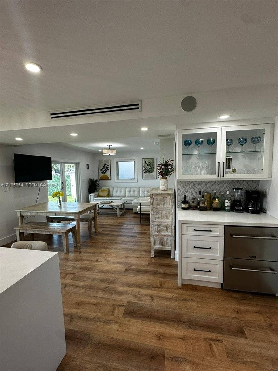 179 Azalea Street, Islamorada, FL 33070 Custom built-in bar featuring white shaker-style cabinetry, glass-front upper displays, stone-pattern backsplash, and stainless-steel under-counter refrigeration, all complemented by wood-finish flooring and recessed lighting