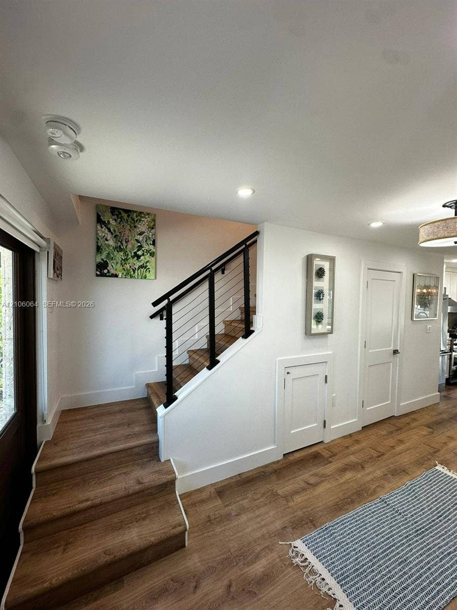 179 Azalea Street, Islamorada, FL 33070 Staircase featuring wood-finish treads, a black metal handrail, and horizontal cable balusters, complemented by wood-finish flooring, recessed lighting, and white shaker-style doors