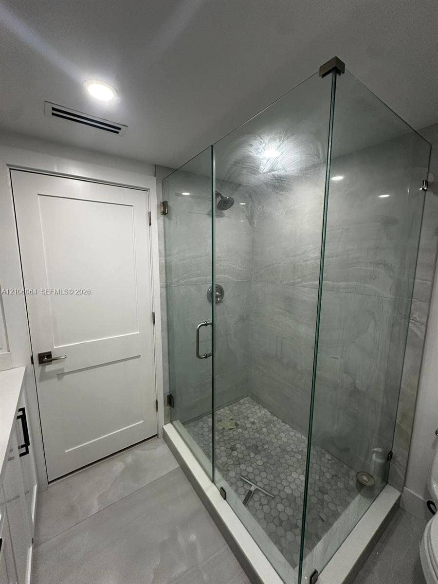 179 Azalea Street, Islamorada, FL 33070 Walk-in shower featuring a frameless glass enclosure, floor-to-ceiling stone-patterned tile surround, and mosaic tile flooring