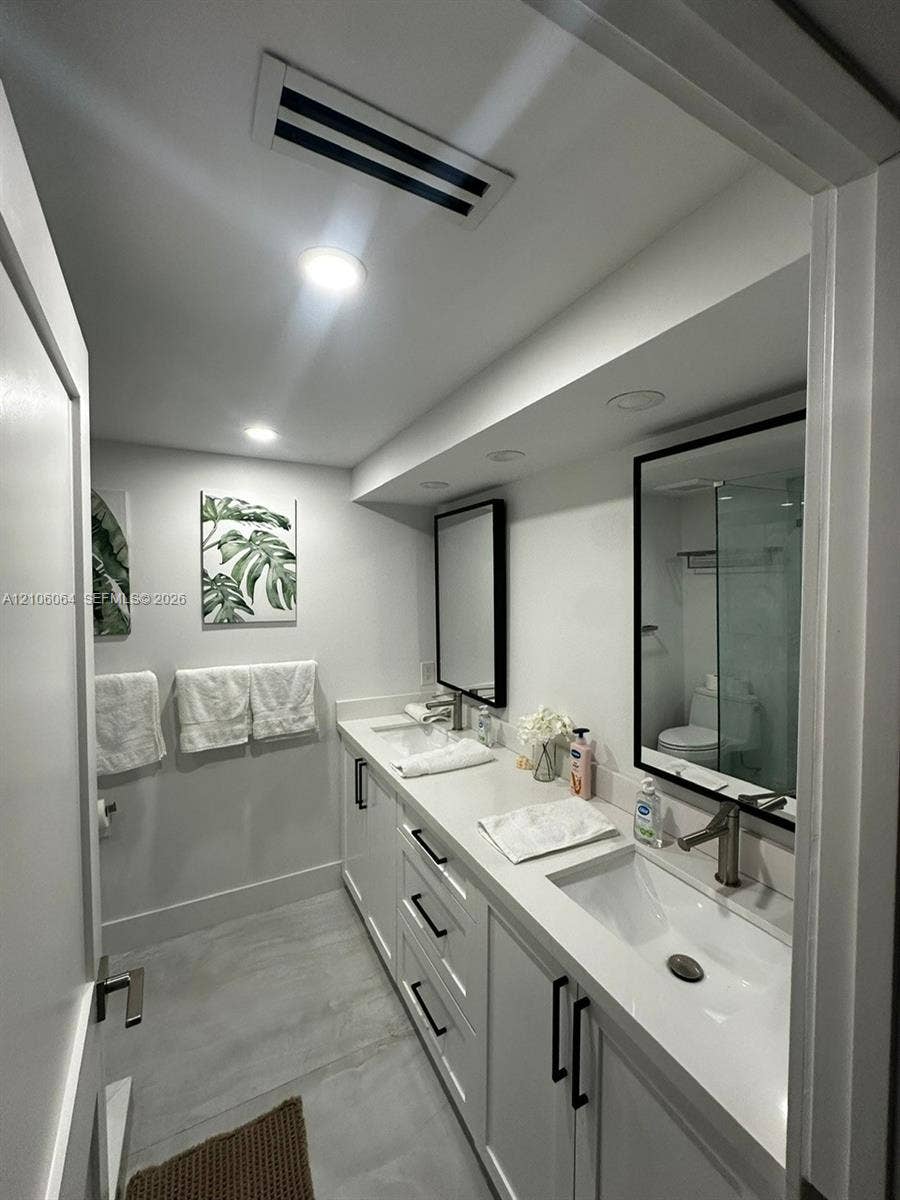 179 Azalea Street, Islamorada, FL 33070 Dual-sink vanity featuring white cabinetry, solid-surface countertops, integrated rectangular basins, and matte black fixtures, complemented by recessed lighting and framed vanity mirrors