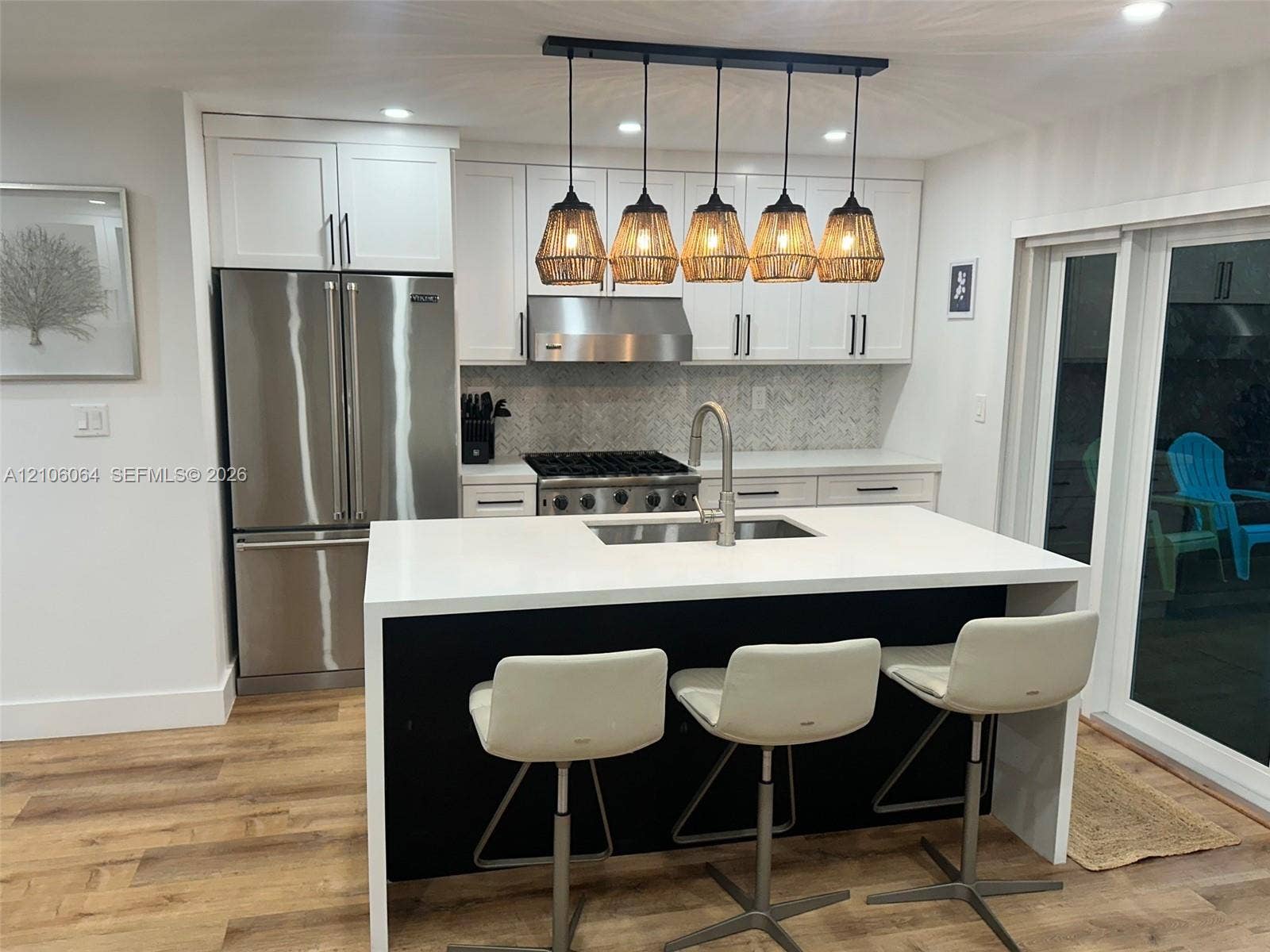 179 Azalea Street, Islamorada, FL 33070 Kitchen featuring a central island with a solid surface countertop, white shaker-style cabinetry, stainless steel appliances, a herringbone tile backsplash, and a five-light hanging pendant fixture