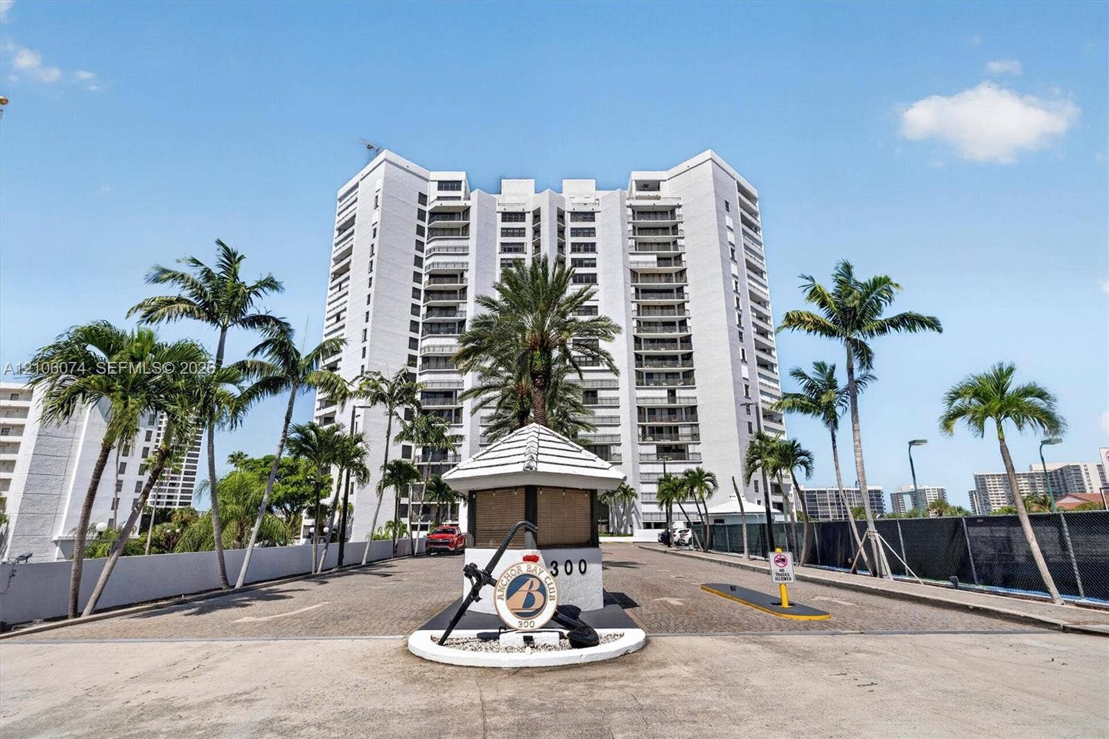 300 Three Islands Boulevard, #308, Hallandale Beach, Hallandale Beach, FL 33009 Multi-story residential high-rise featuring a secure gated entrance with guardhouse, paved arrival area, and mature palm landscaping