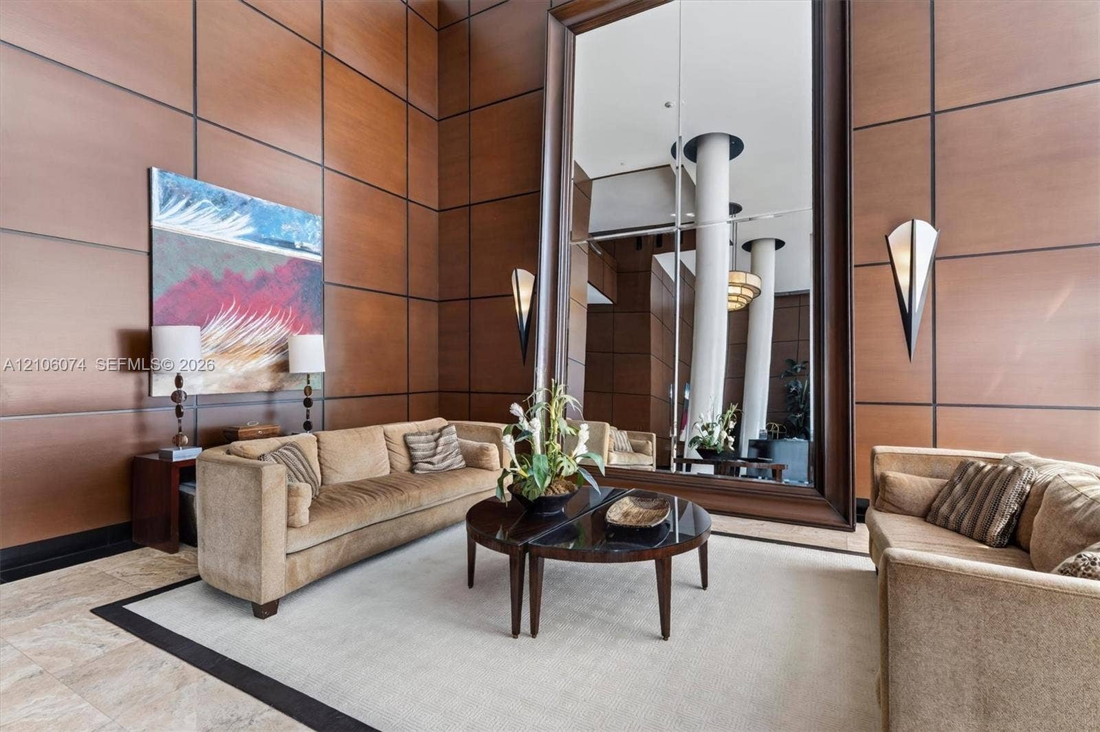 300 Three Islands Boulevard, #308, Hallandale Beach, Hallandale Beach, FL 33009 Double-height interior featuring wood-panelled wall treatments, oversized framed mirror, and integrated triangular wall sconces