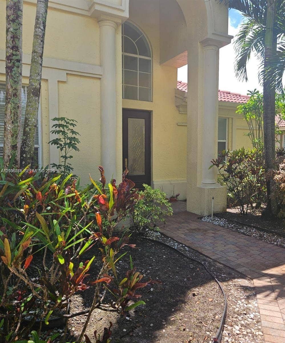 13382 Lakepointe Circle, #0, Cooper City, Cooper City, FL 33330 Stucco exterior featuring dual architectural columns, a tiled roof, a central arched entryway with a glass-paneled door, and a brick-paver walkway