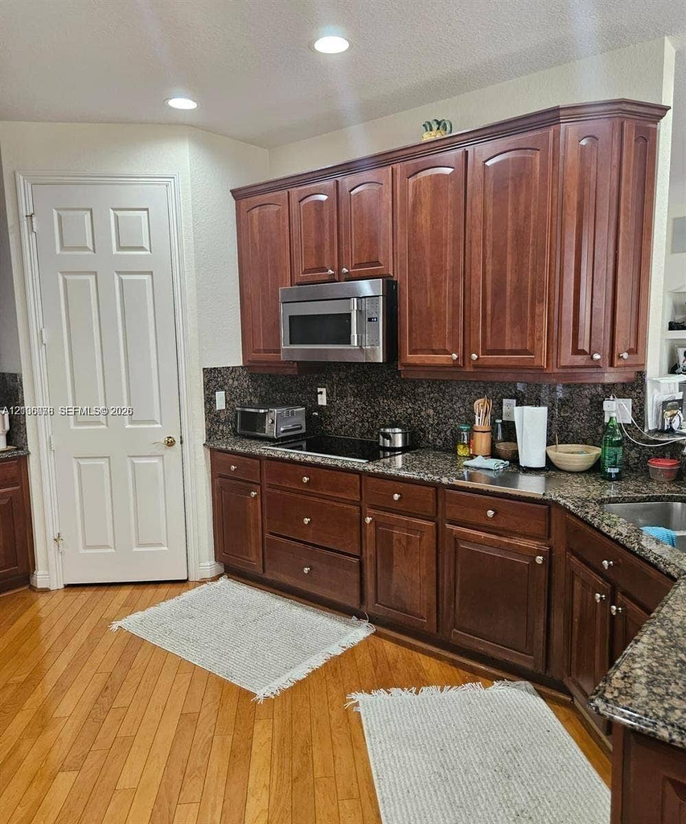 13382 Lakepointe Circle, #0, Cooper City, Cooper City, FL 33330 Kitchen featuring wood cabinetry, stone countertops, built-in stainless steel microwave, integrated cooktop, and wood-finish flooring