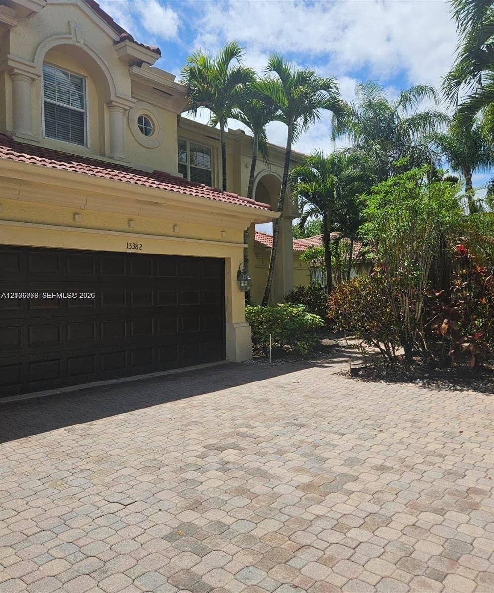 13382 Lakepointe Circle, #0, Cooper City, Cooper City, FL 33330 Mediterranean-inspired exterior featuring a multi-level facade, arched window detailing, a recessed garage door, and a multi-toned paver driveway