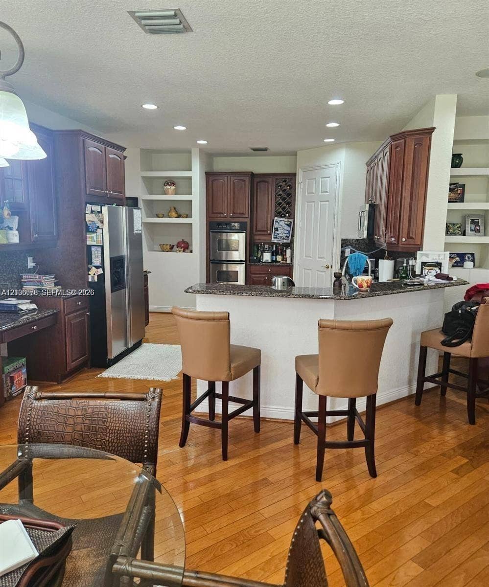 13382 Lakepointe Circle, #0, Cooper City, Cooper City, FL 33330 Kitchen featuring dark-stained wooden cabinetry, stone countertops, stainless steel appliances including a double wall oven, wood-finish flooring, and integrated display shelving