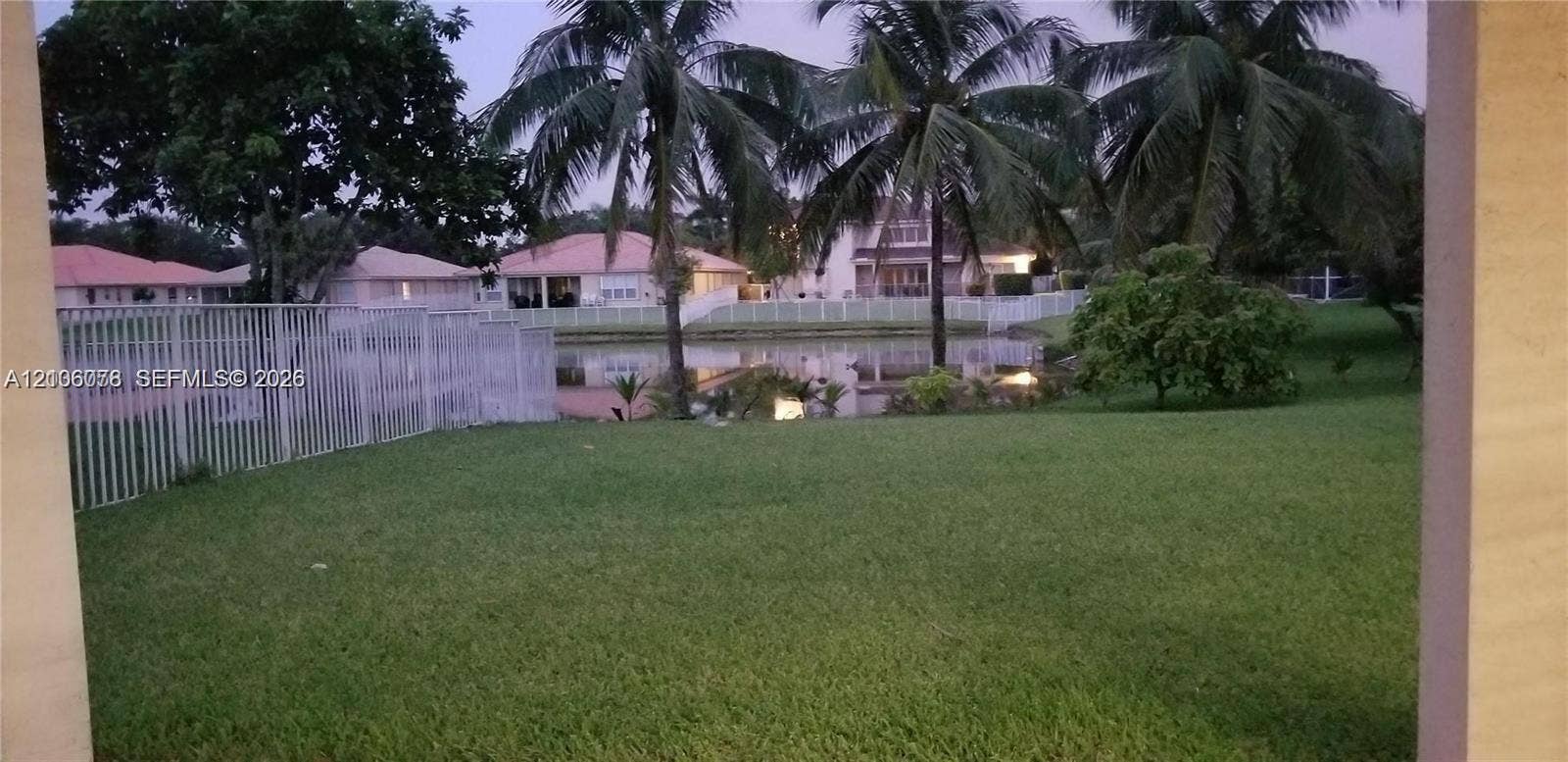 13382 Lakepointe Circle, #0, Cooper City, Cooper City, FL 33330 Expansive backyard featuring a grass lawn, mature palm trees, perimeter metal fencing, and a body of water