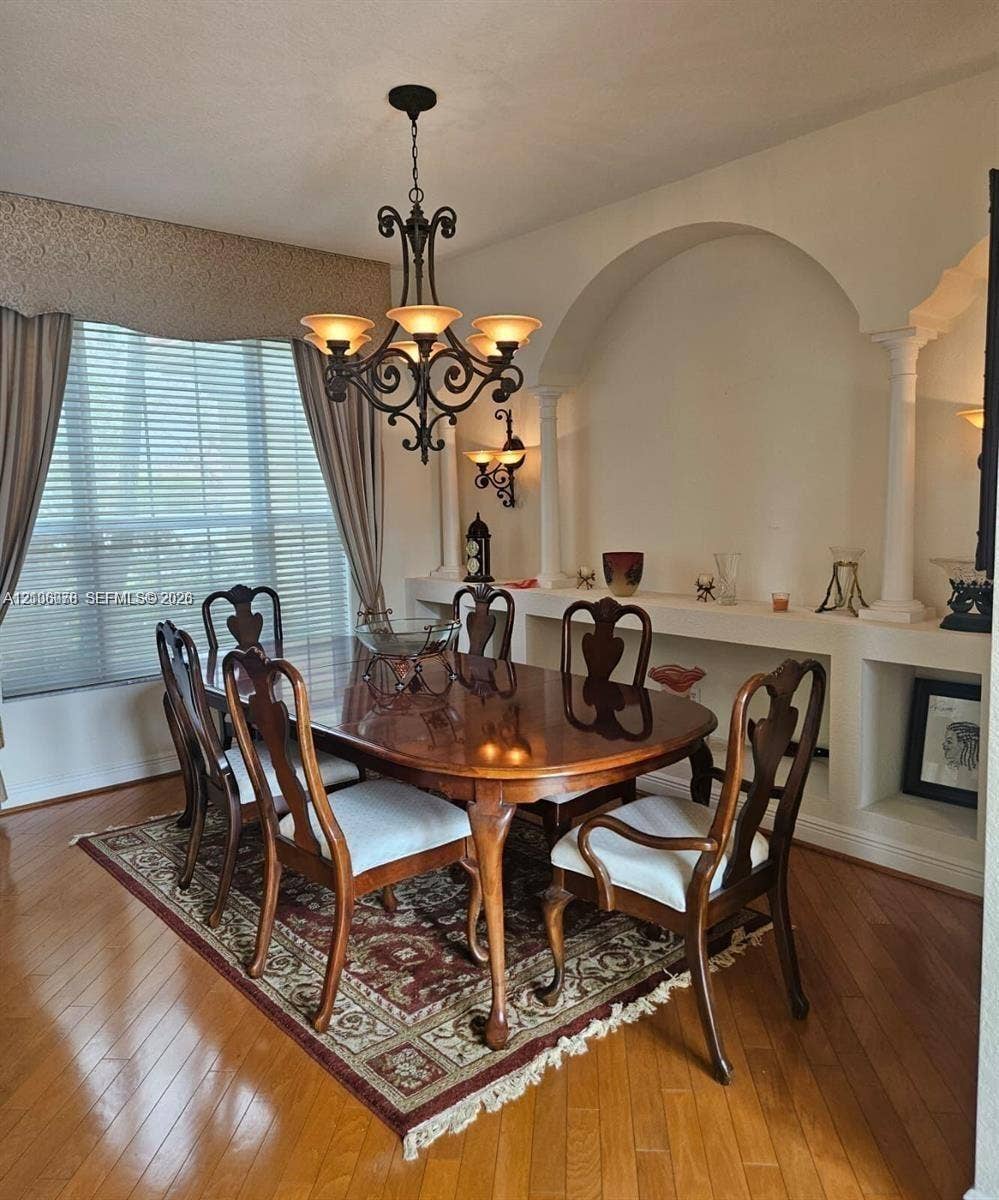 13382 Lakepointe Circle, #0, Cooper City, Cooper City, FL 33330 Dining space featuring wood-finish flooring, a decorative arched wall niche with classical column accents, and an ornate wrought-iron chandelier